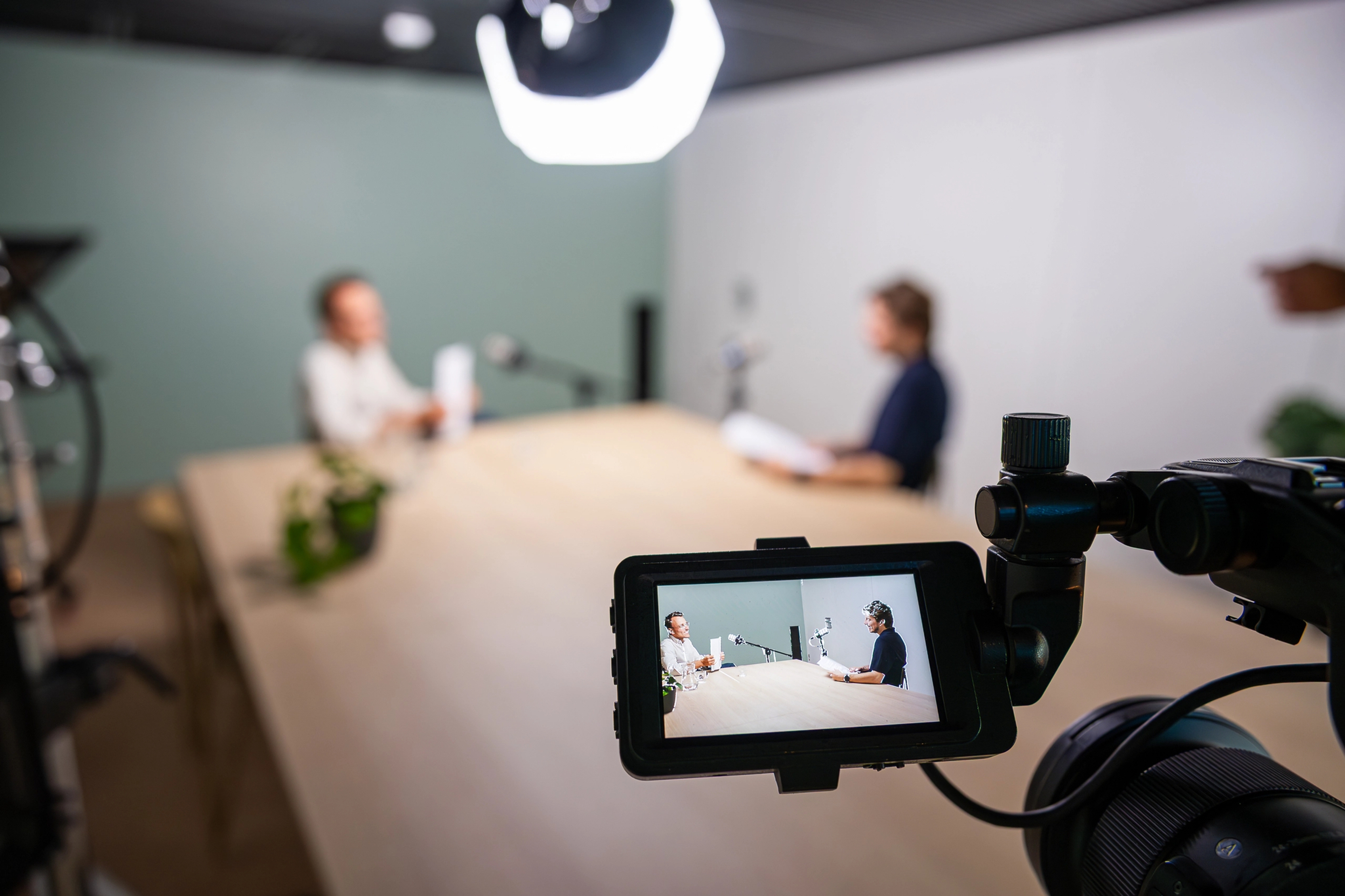 2 mannen aan een tafel bij de opname van het webinar, we zijn hen scherp in beeld in het scherm van de camera.van