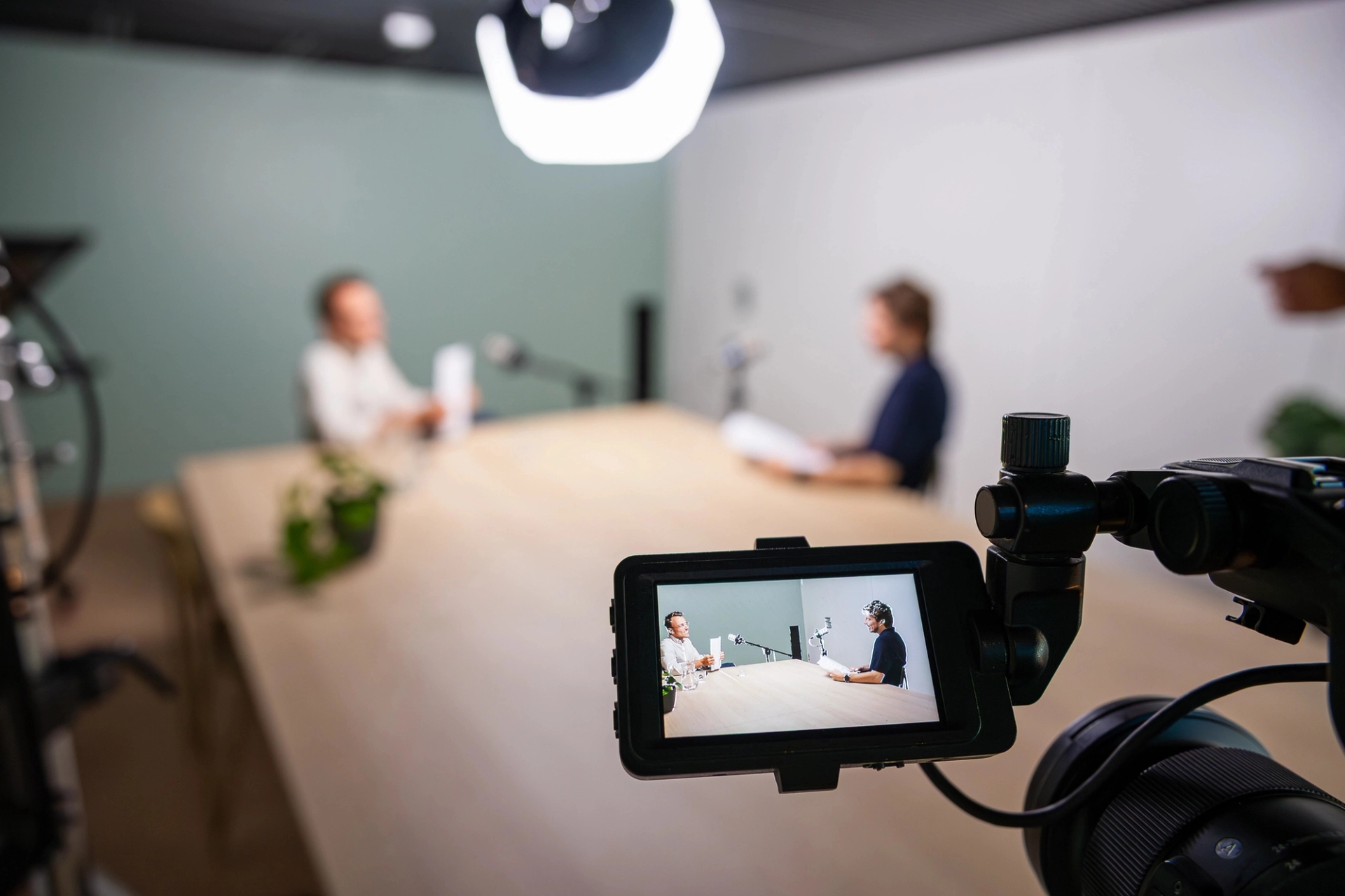 2 mannen aan een tafel bij de opname van het webinar, we zijn hen scherp in beeld in het scherm van de camera.van