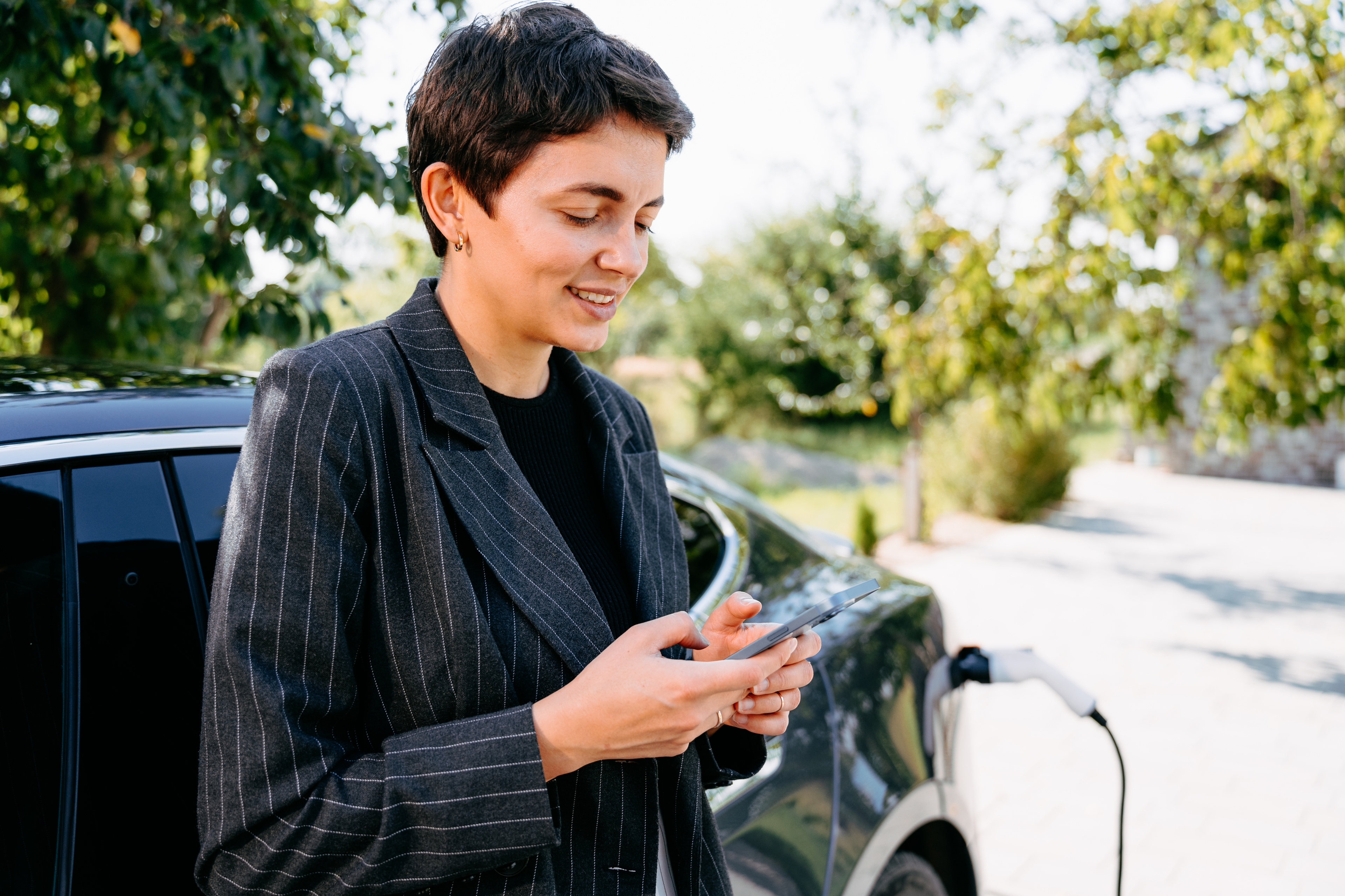 Jonge business vrouw met smartphone in de hand bij haar opladende elektrische wagen