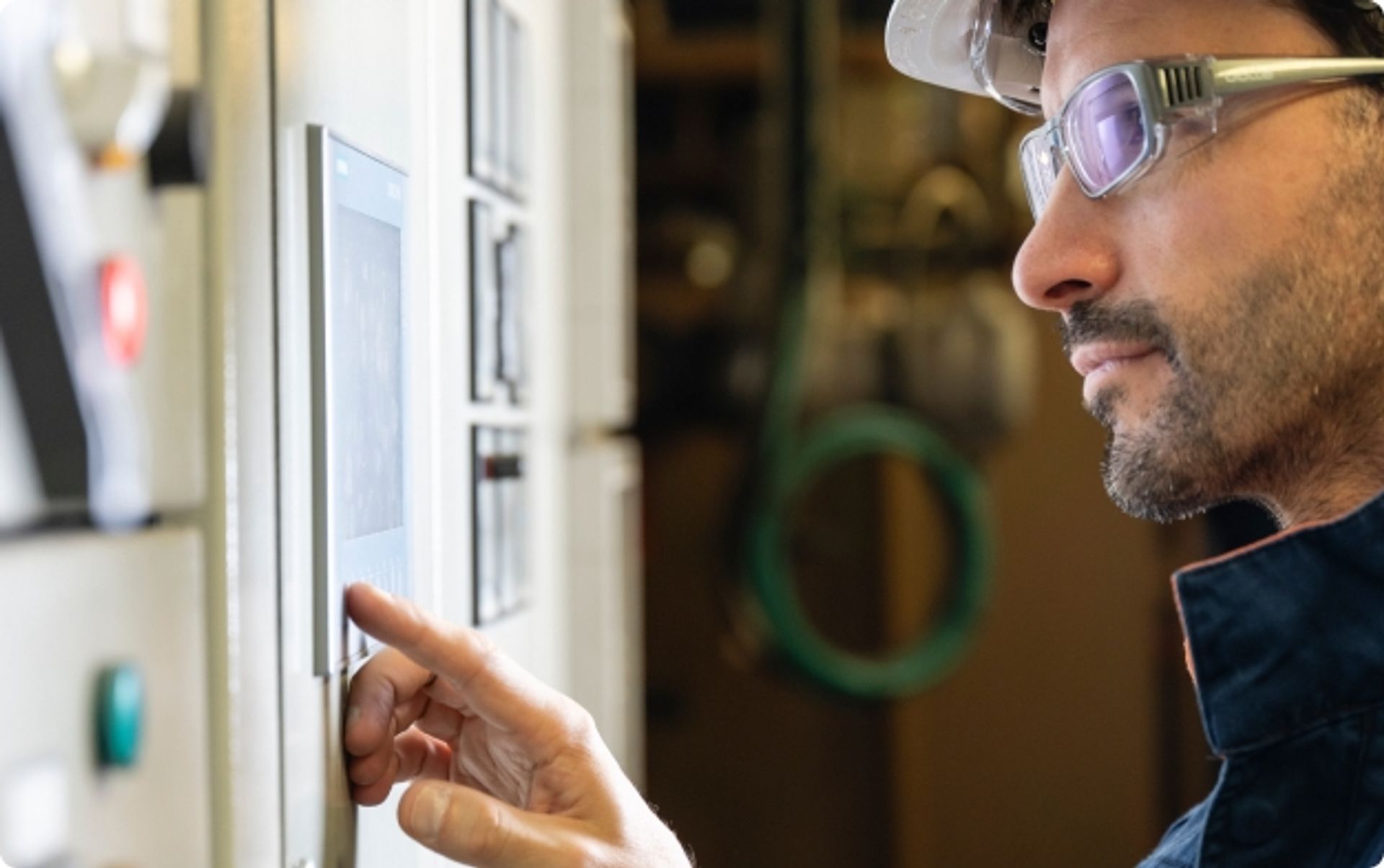 Technicien portant un casque et des lunettes de sécurité, utilisant un écran tactile intégré à un tableau technique