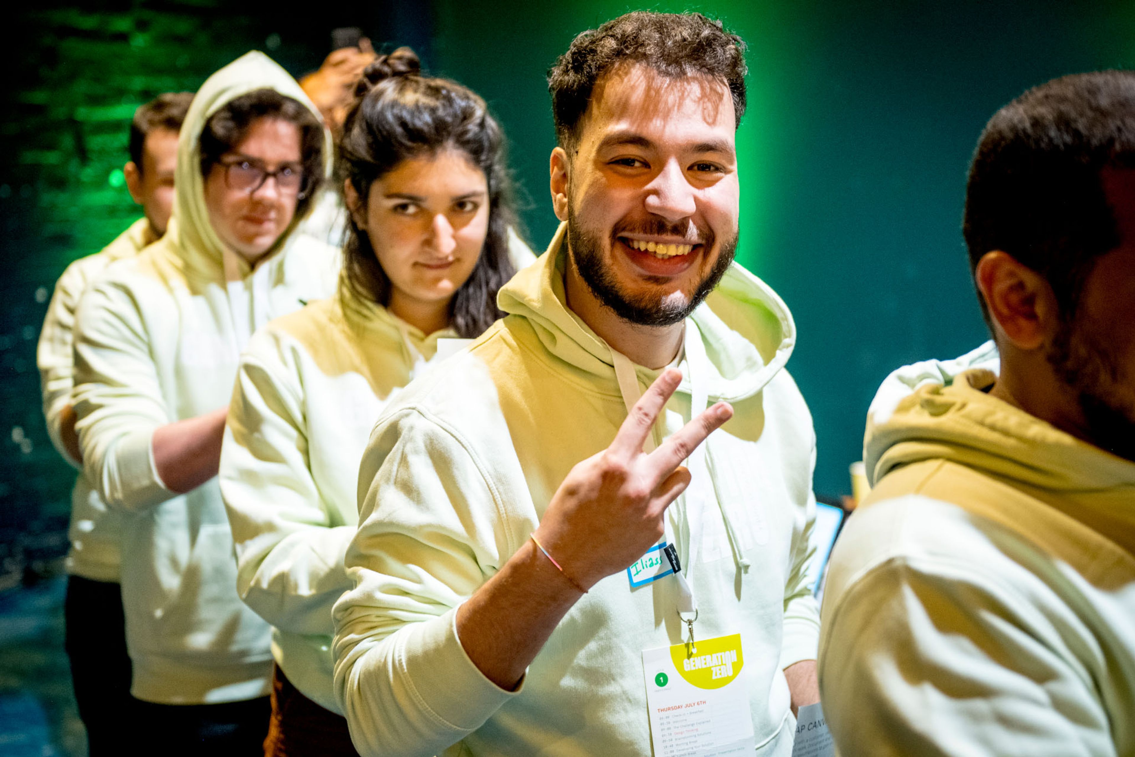 Iliass en 5-tal companen met lichtgele hoodies aan vormen een treintje. Iliass maakt het peace teken.