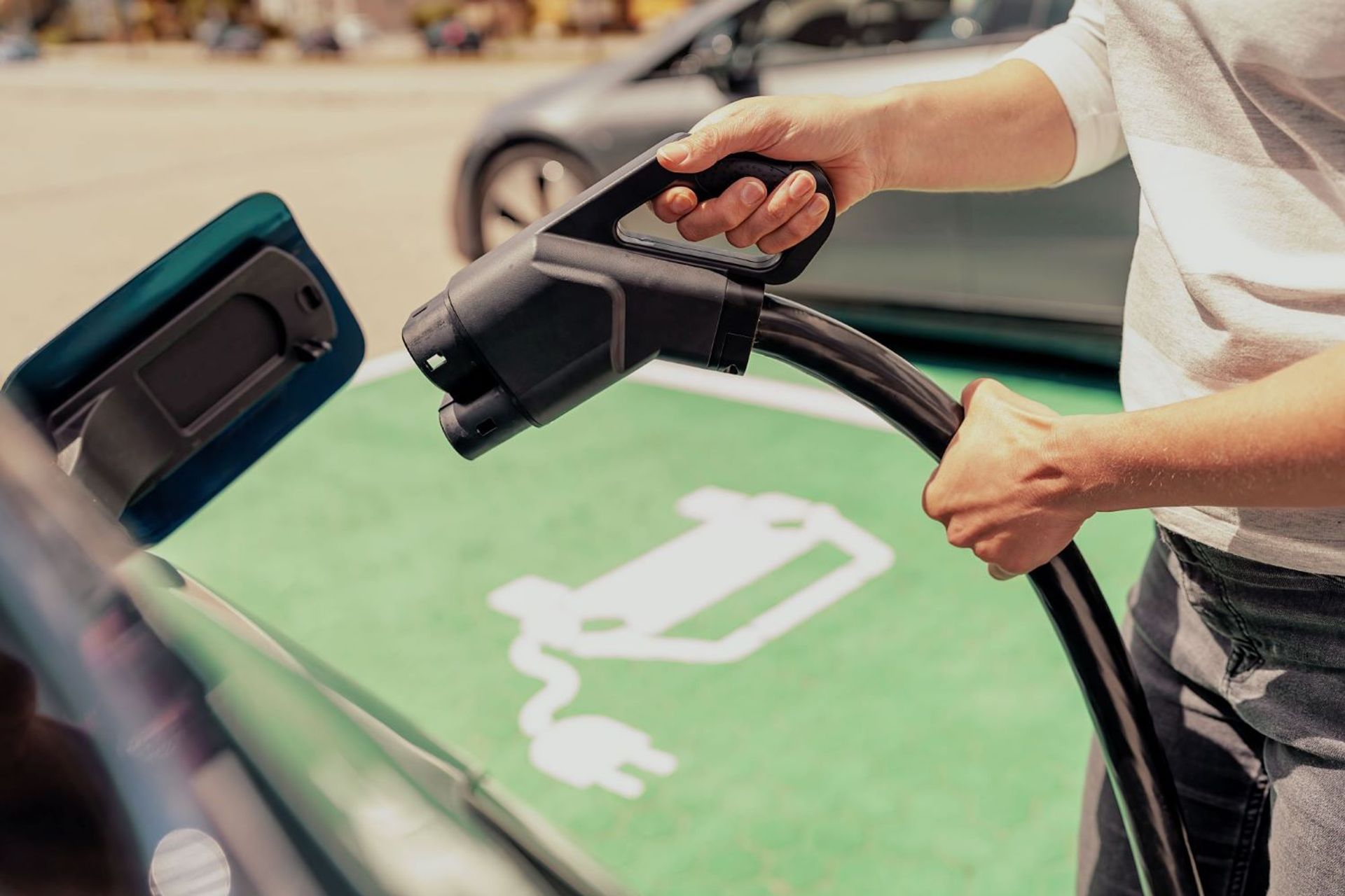 Dame gaat net de stekker in haar elektrische wagen steken op een publieke laadplaats.
