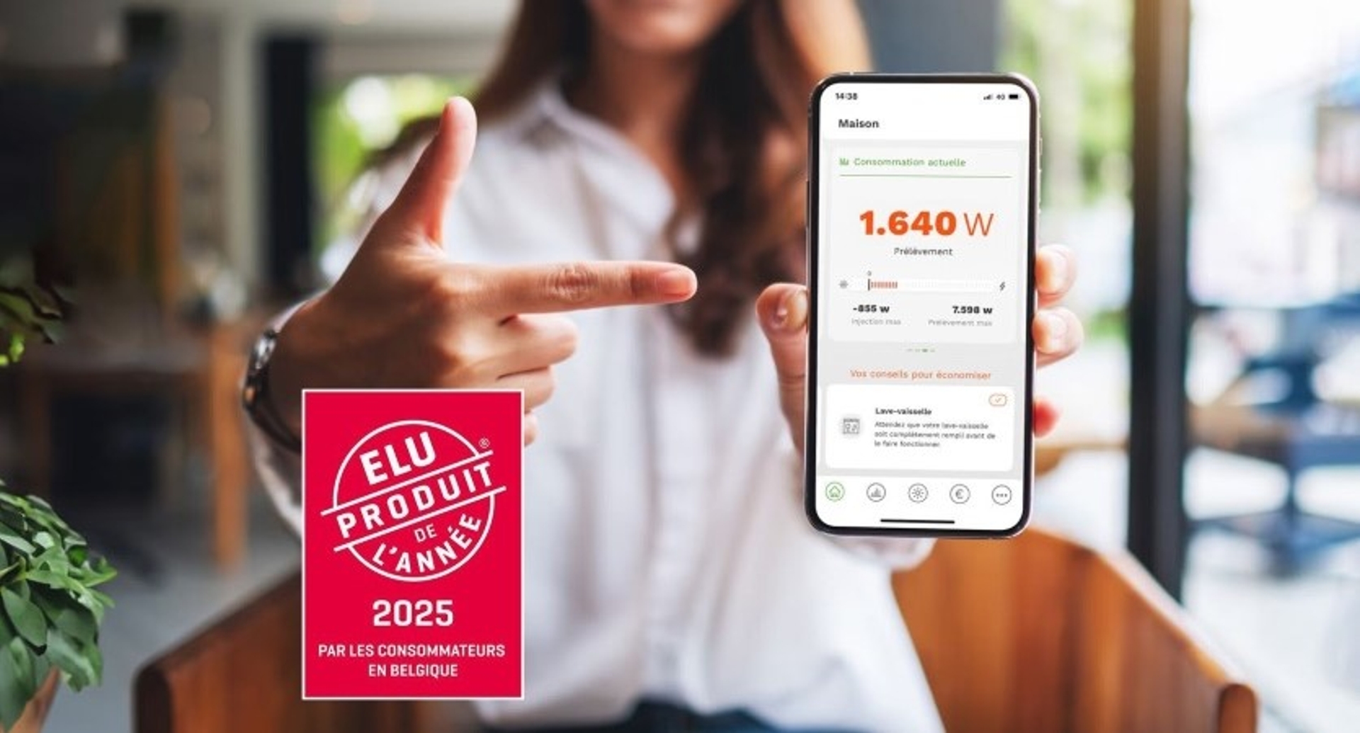 Femme tenant un smartphone affichant une application de suivi de consommation d’énergie, avec un autocollant rouge indiquant ‘Élu produit de l’année 2025 par les consommateurs en Belgique