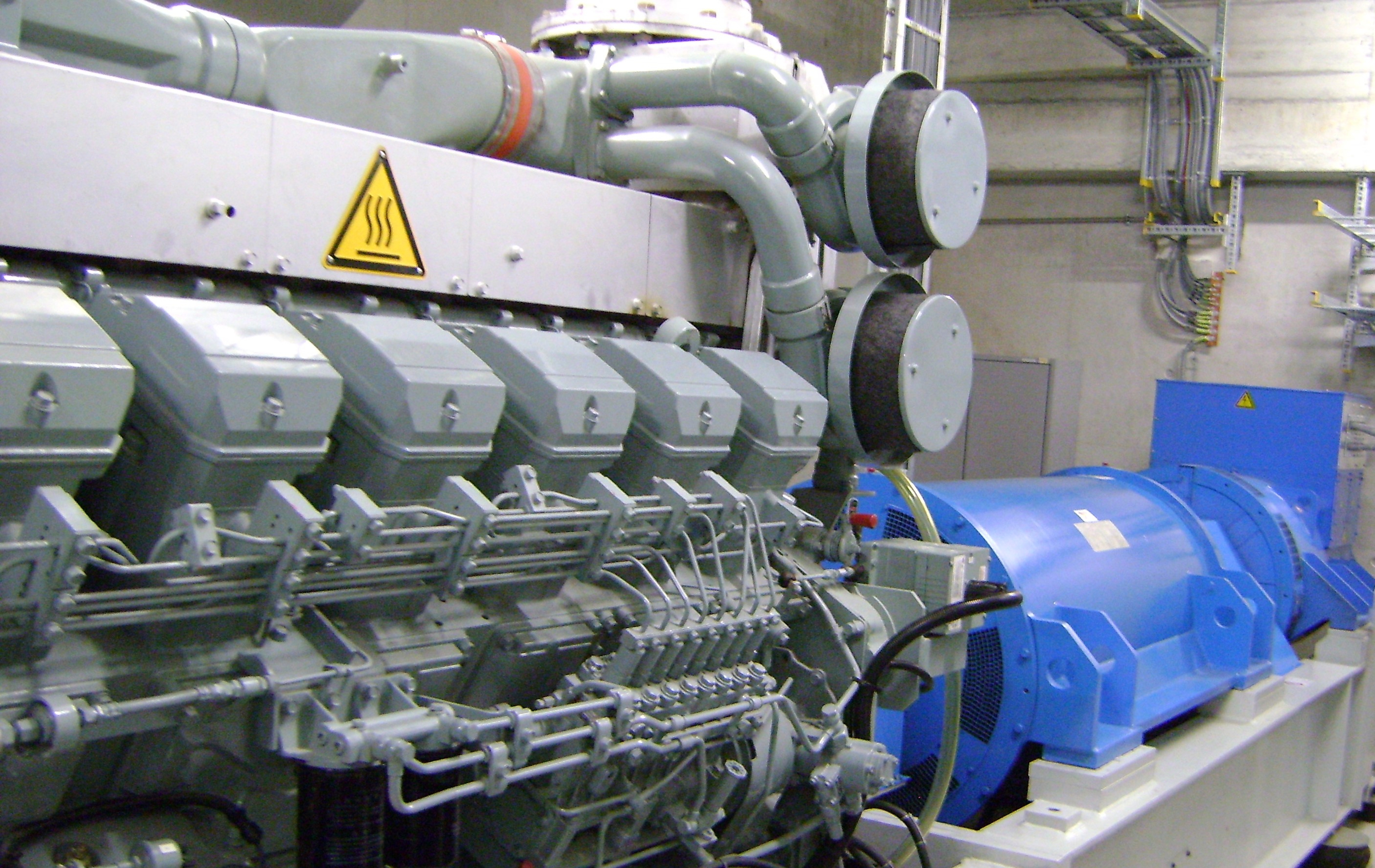 Vue rapprochée d’un moteur industriel de cogénération gris et bleu, équipé de conduites et composants mécaniques, installé dans une centrale technique moderne