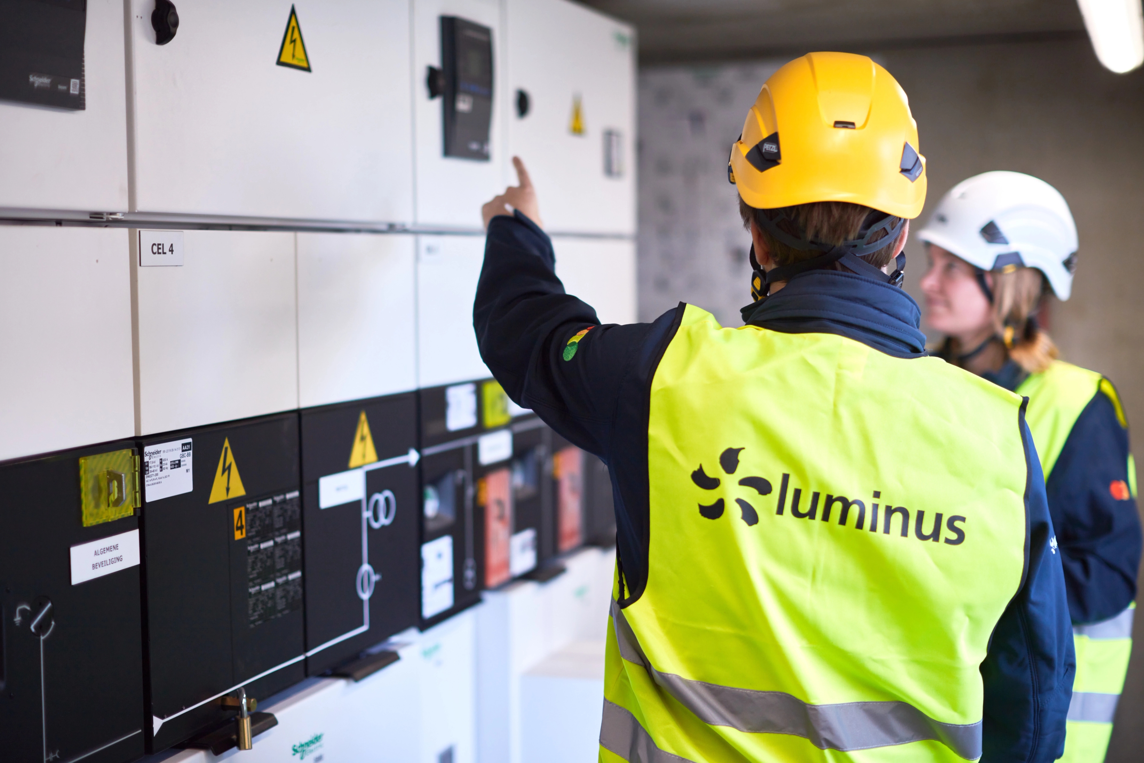 Deux techniciens Luminus inspectent un tableau électrique industriel dans le cadre d'un contrôle de qualité énergétique
