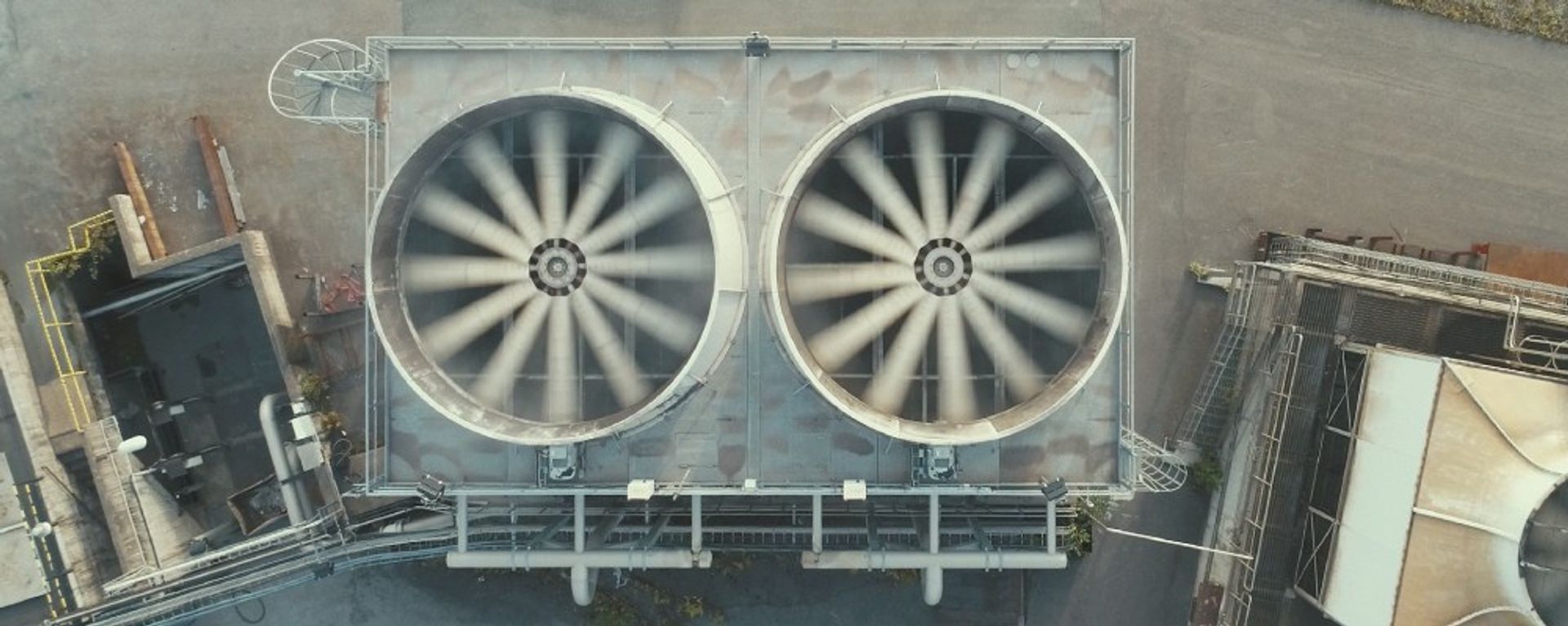 2 draaiende ventilatoren van een turbine op een bedrijfsterrein, gezien van boven af.