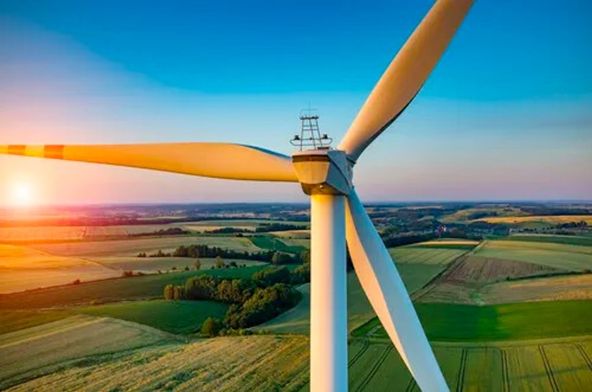 Gros plan sur une éolienne au-dessus d'un paysage agricole au coucher du soleil