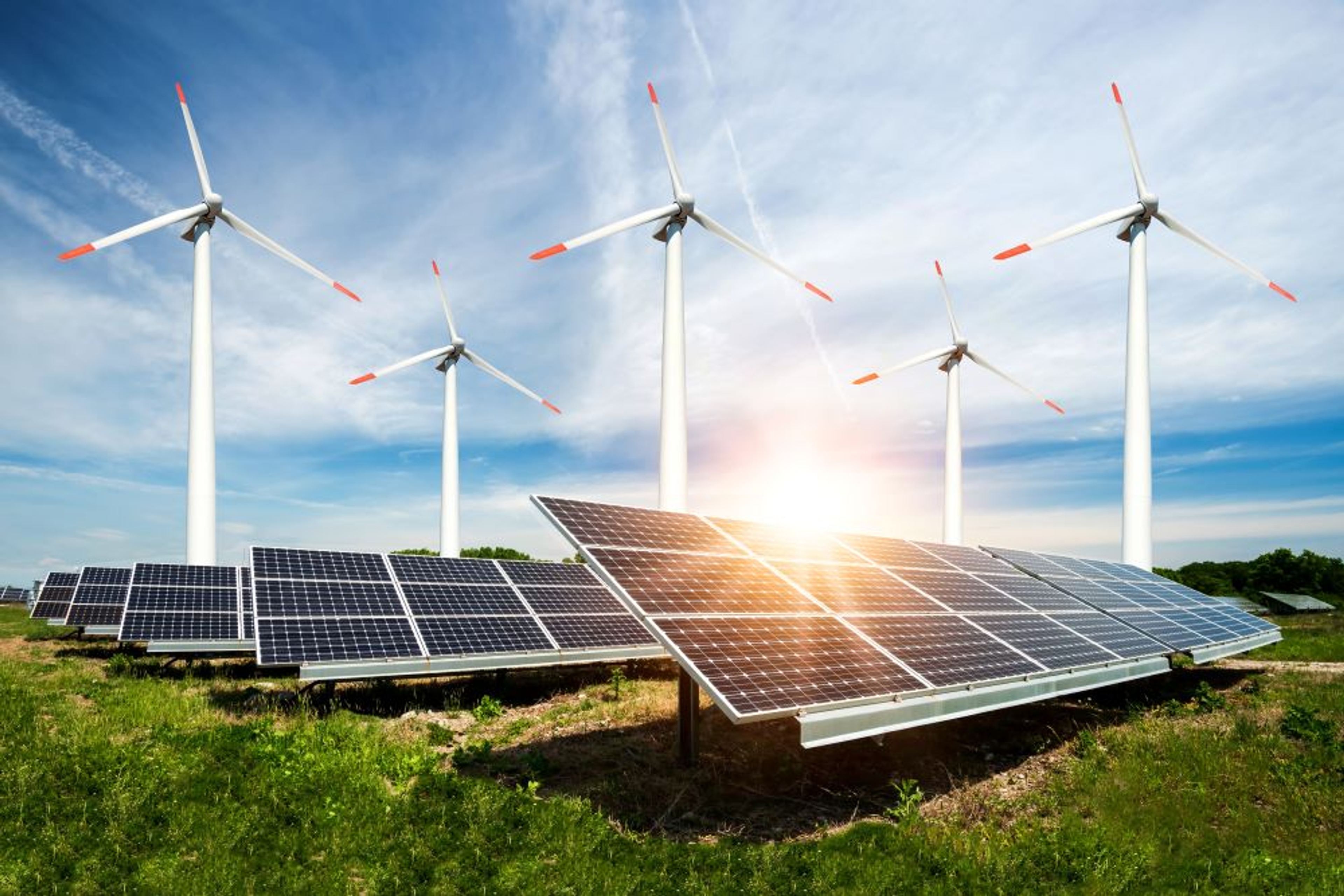 5 windturbines achter een veld zonnepanelen tegen de blauwe lucht.