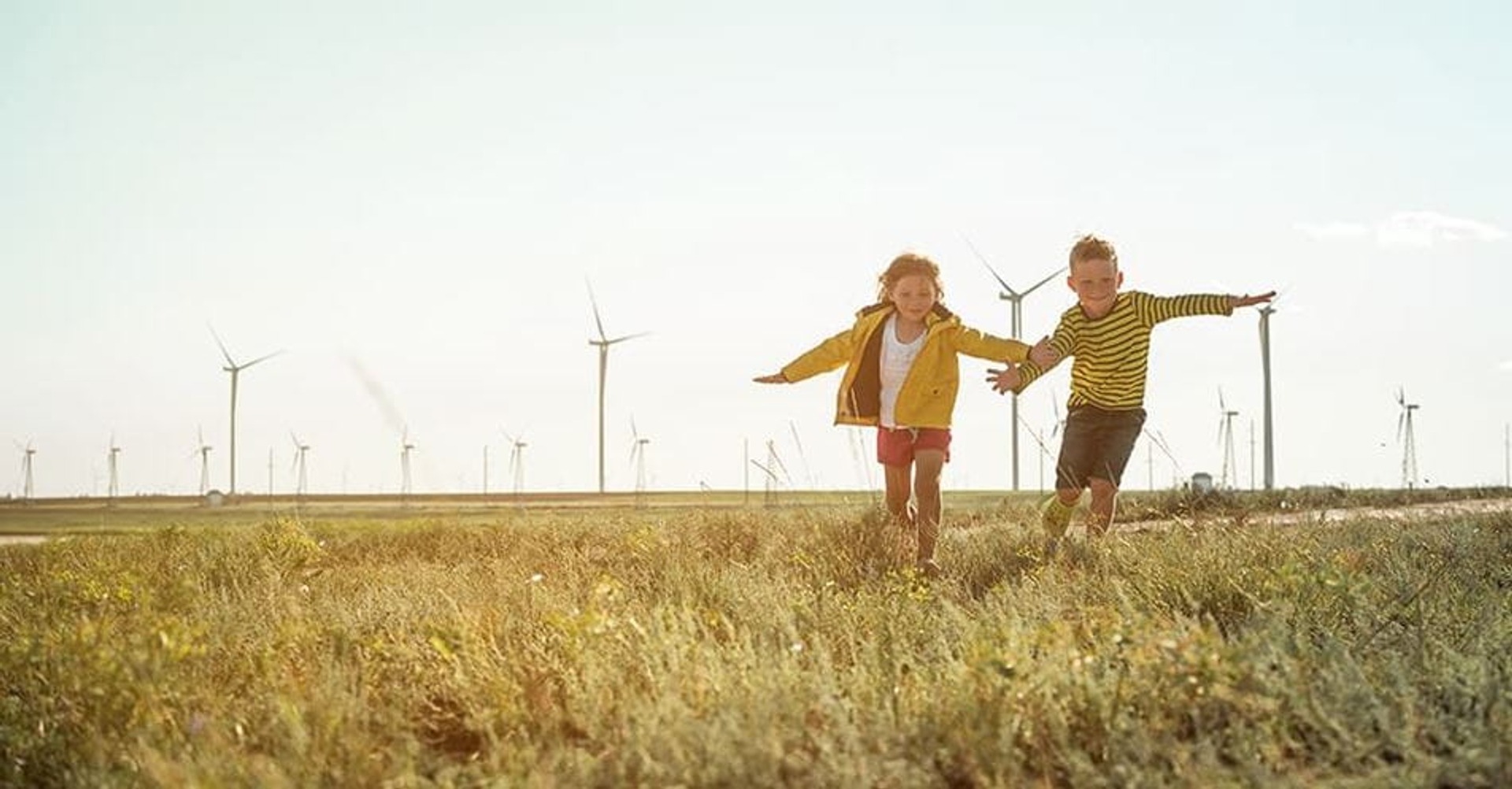 Deux enfants qui courent devant un parc éolien