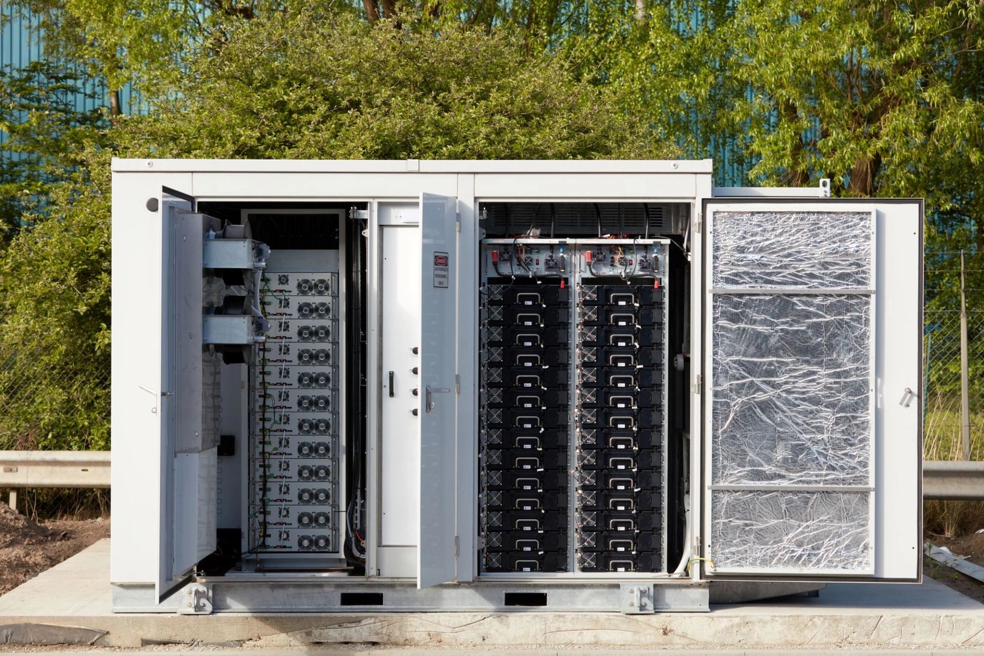 Industriële batterij waarvan de deuren openstaan, groene struiken in de achtergond.