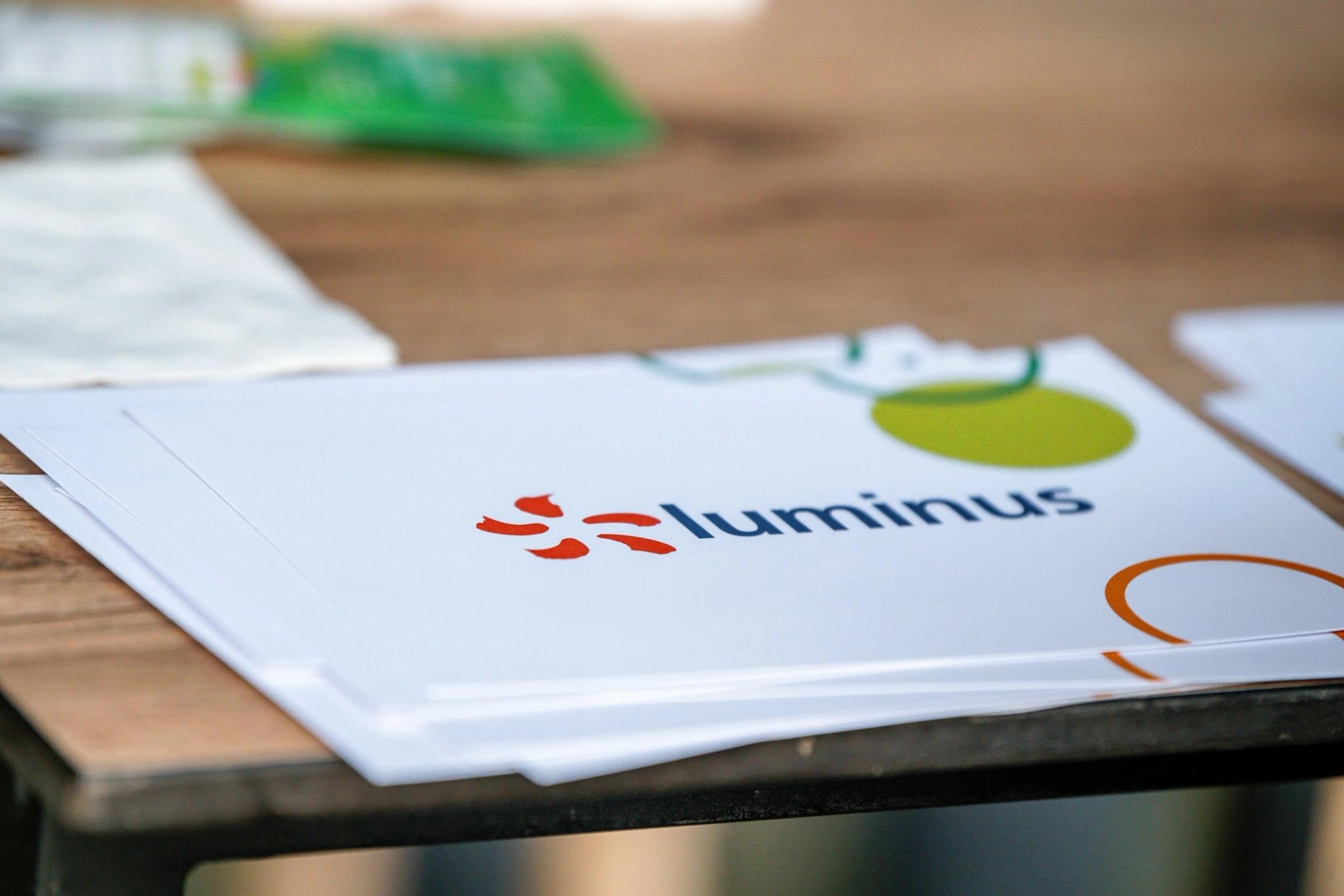Een stapel witte papieren met het logo en de tekst ‘Luminus’ in blauw en een oranje ontwerp op een houten tafel, wat een professionele, strakke uitstraling geeft.
