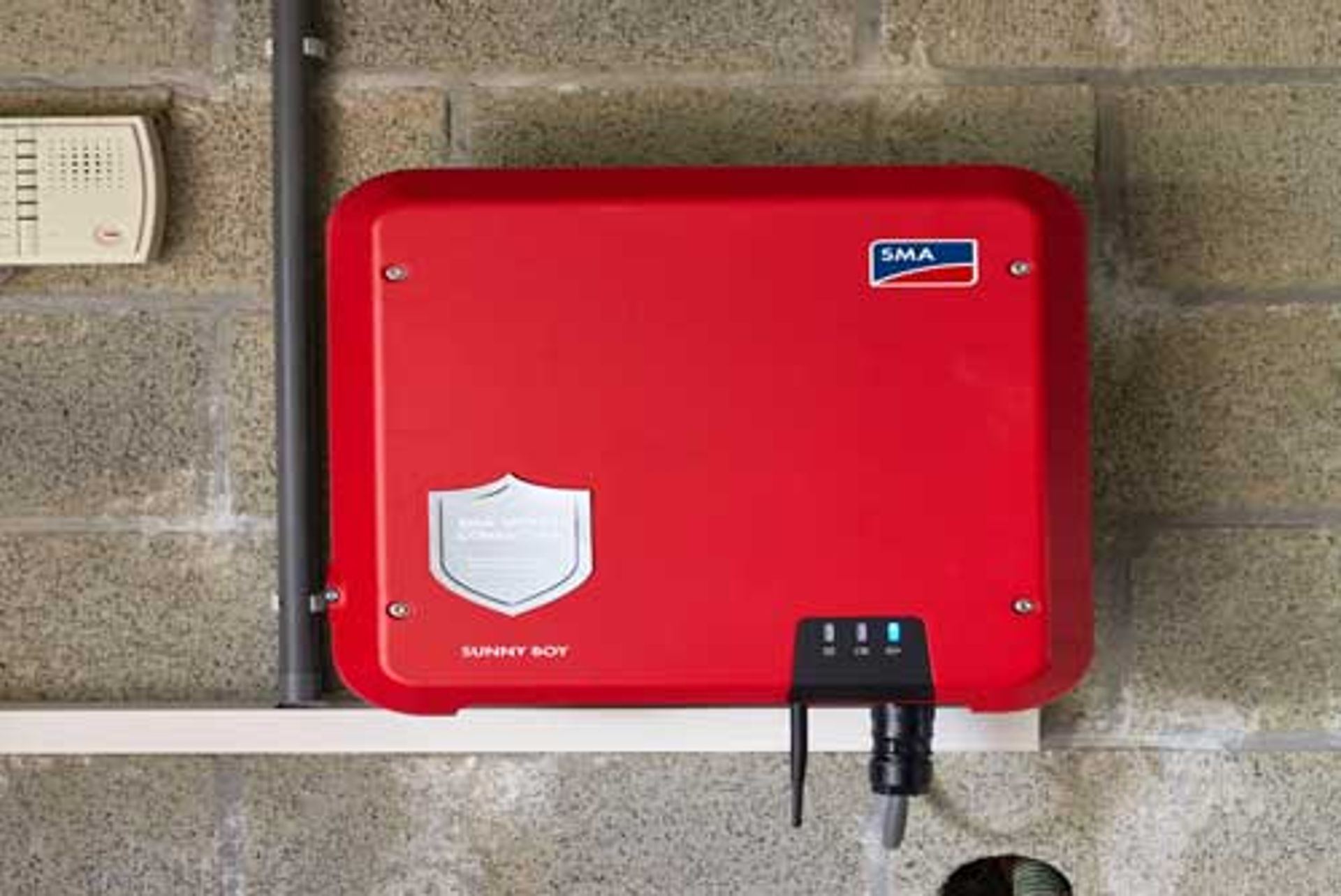 Onduleur solaire rouge de marque fixé sur un mur en briques
