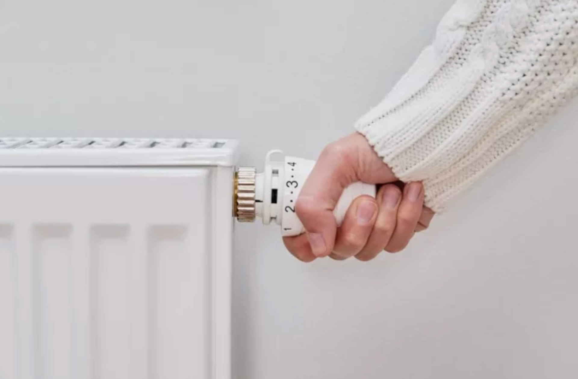 witte radiator met hand aan de thermostaatknop, witte gebreide trui.