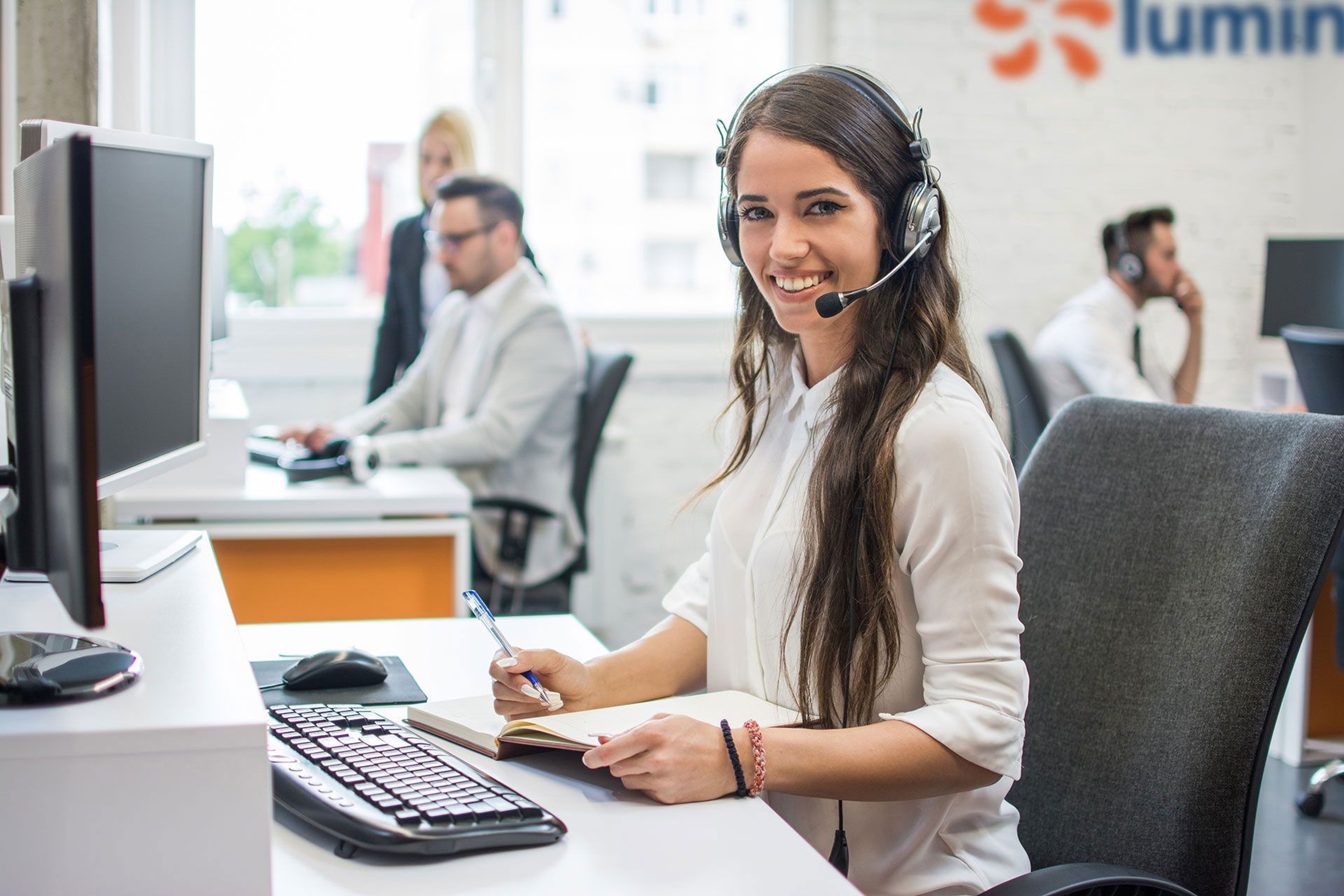 Conseillère du service client portant un casque micro, souriante devant son bureau, dans un centre d’appel moderne