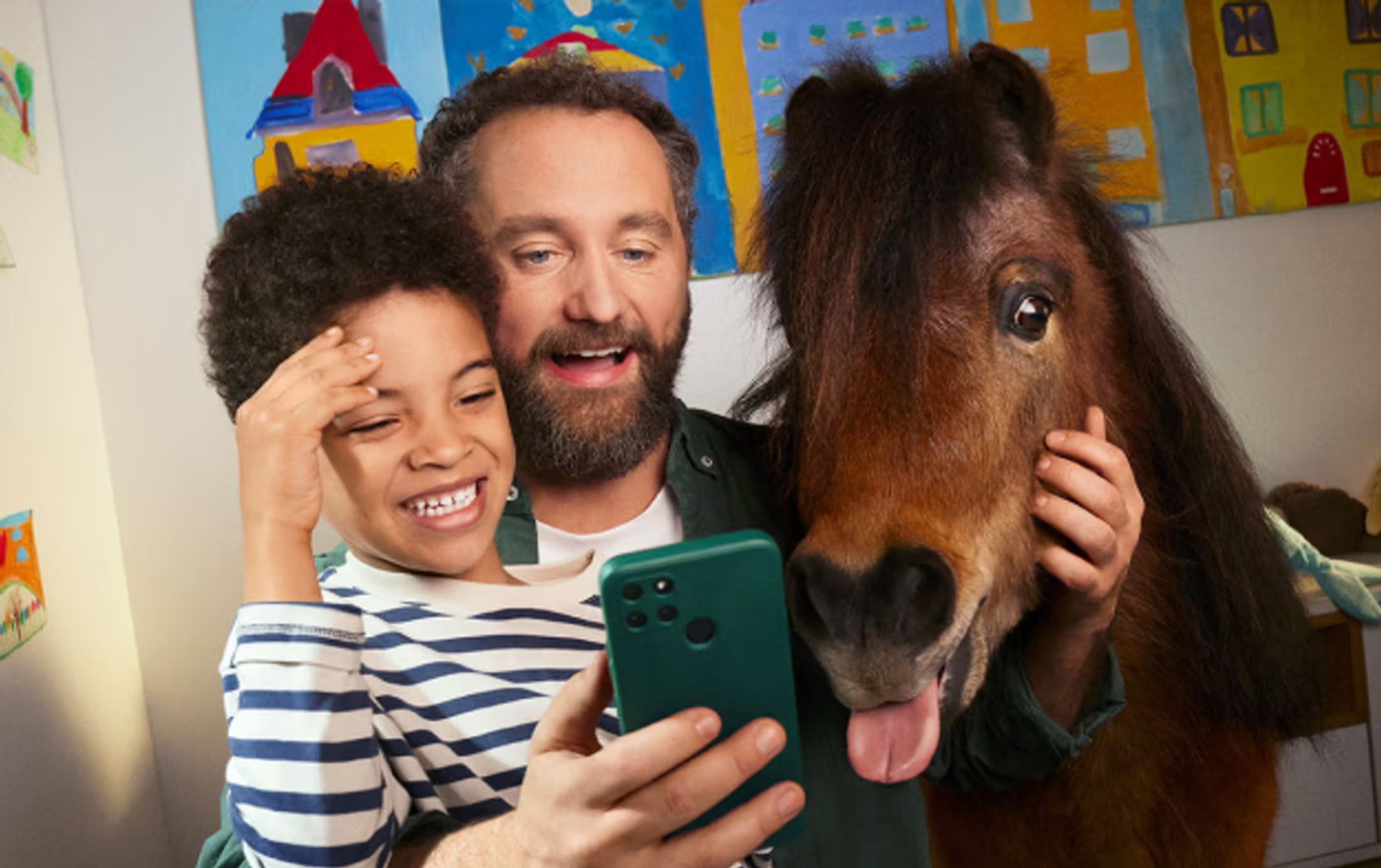 Un homme, un enfant et un poney regardent ensemble l’écran d’un smartphone