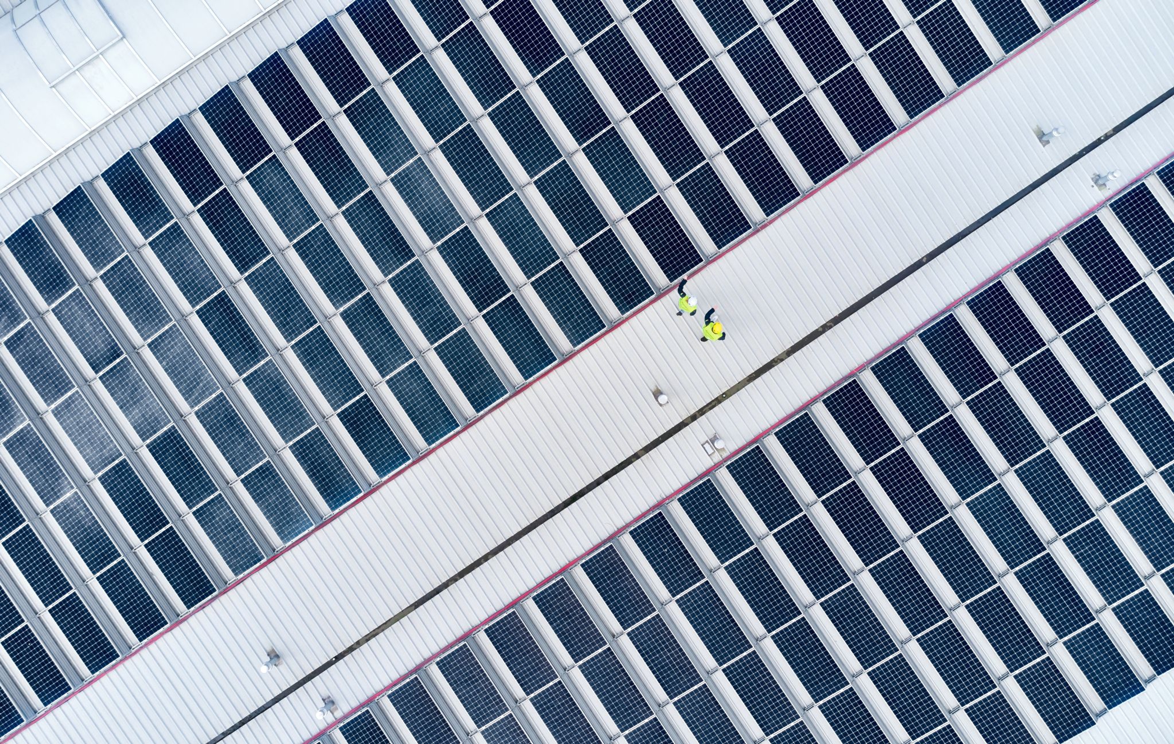 Bovenaanzicht van een groot dak vol zonnepanelen. 2 personen zijn kleine fluo gele stipjes op het dak.