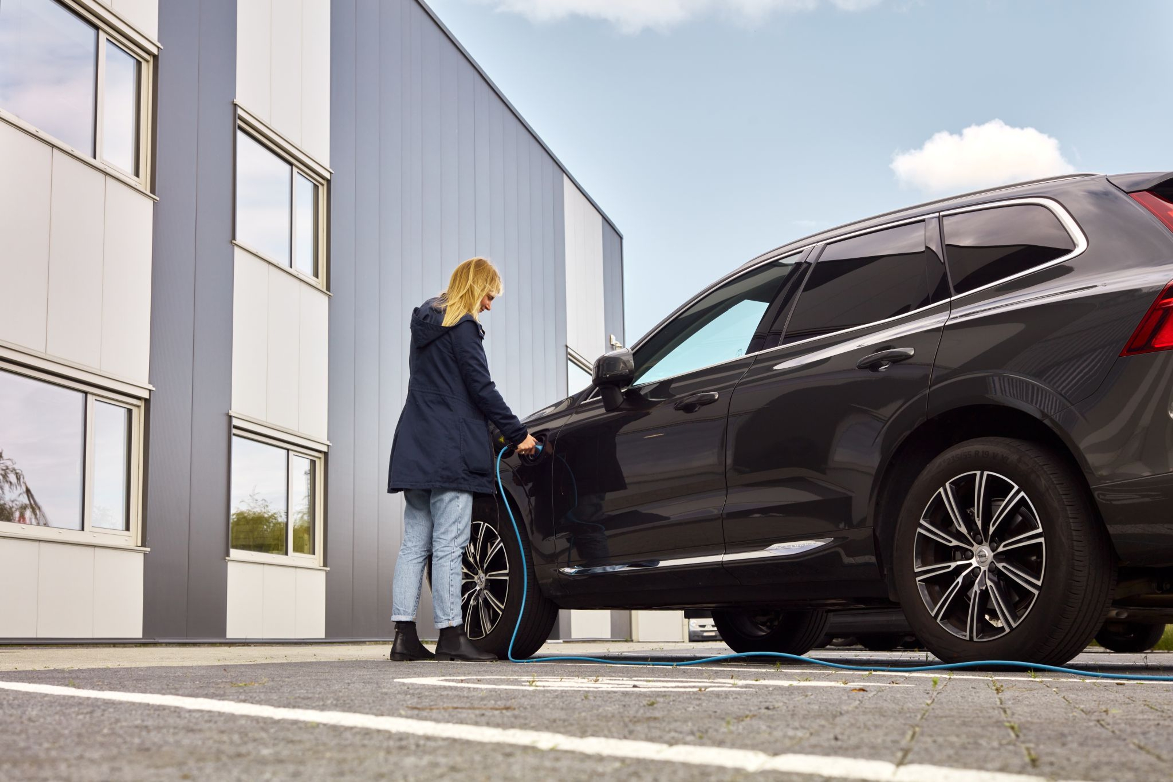 Blonde dame laadt haar grote zwarte wagen op aan een kantoorgebouw