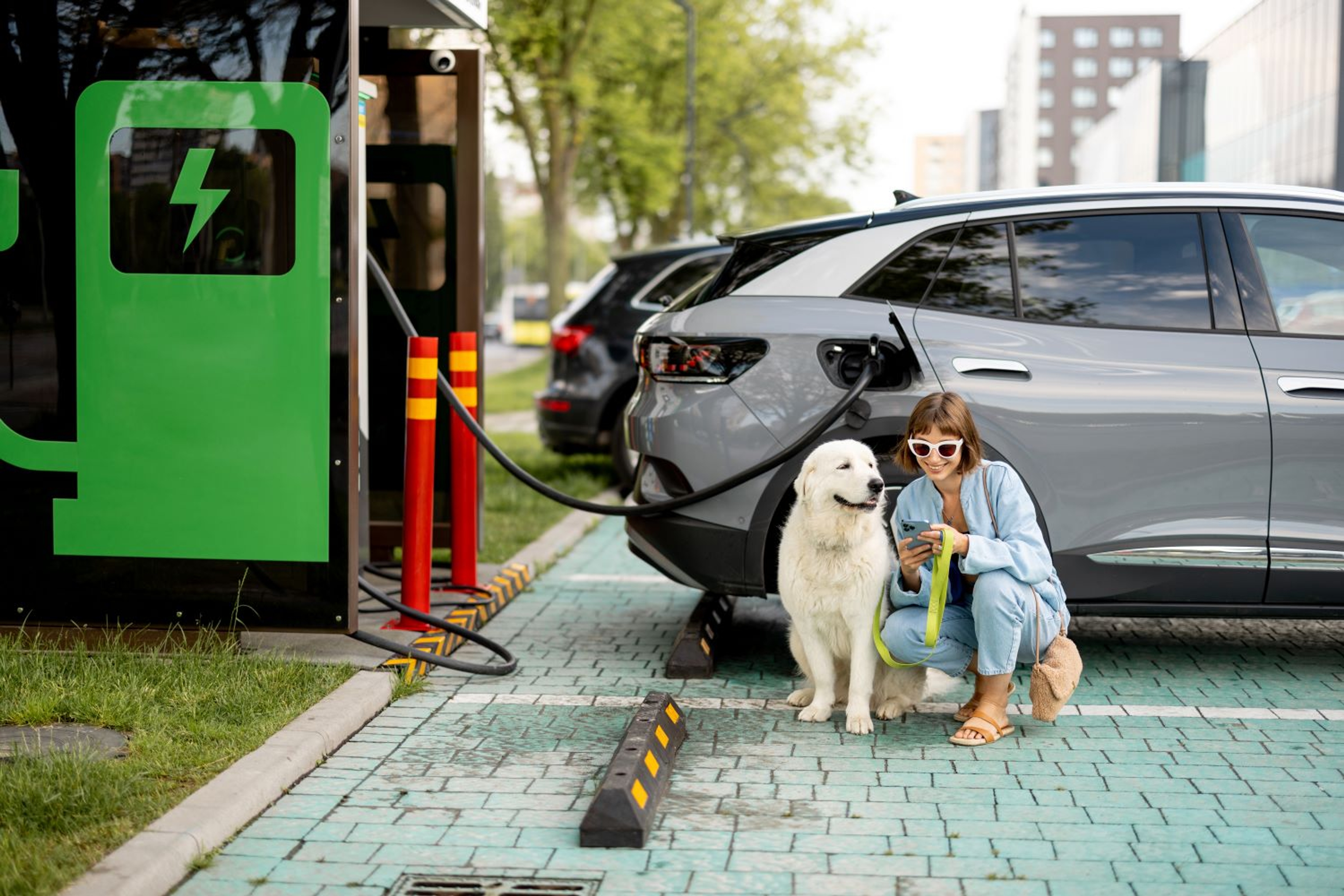 Femme assise avec son chien à côté d’une voiture électrique en charge sur une borne publique