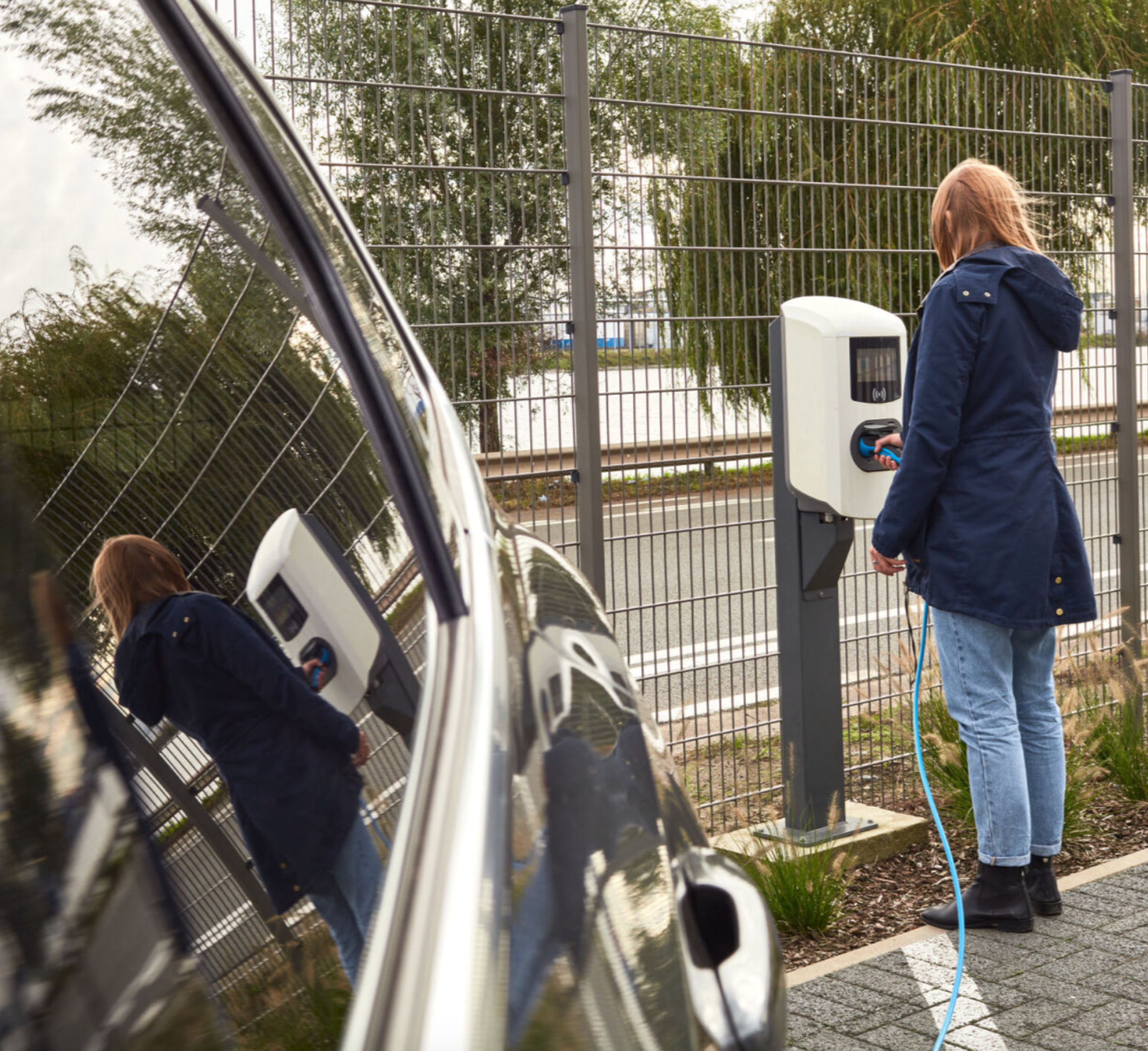 Personne branchant une voiture électrique sur une borne de recharge installée sur un parking d'entreprise