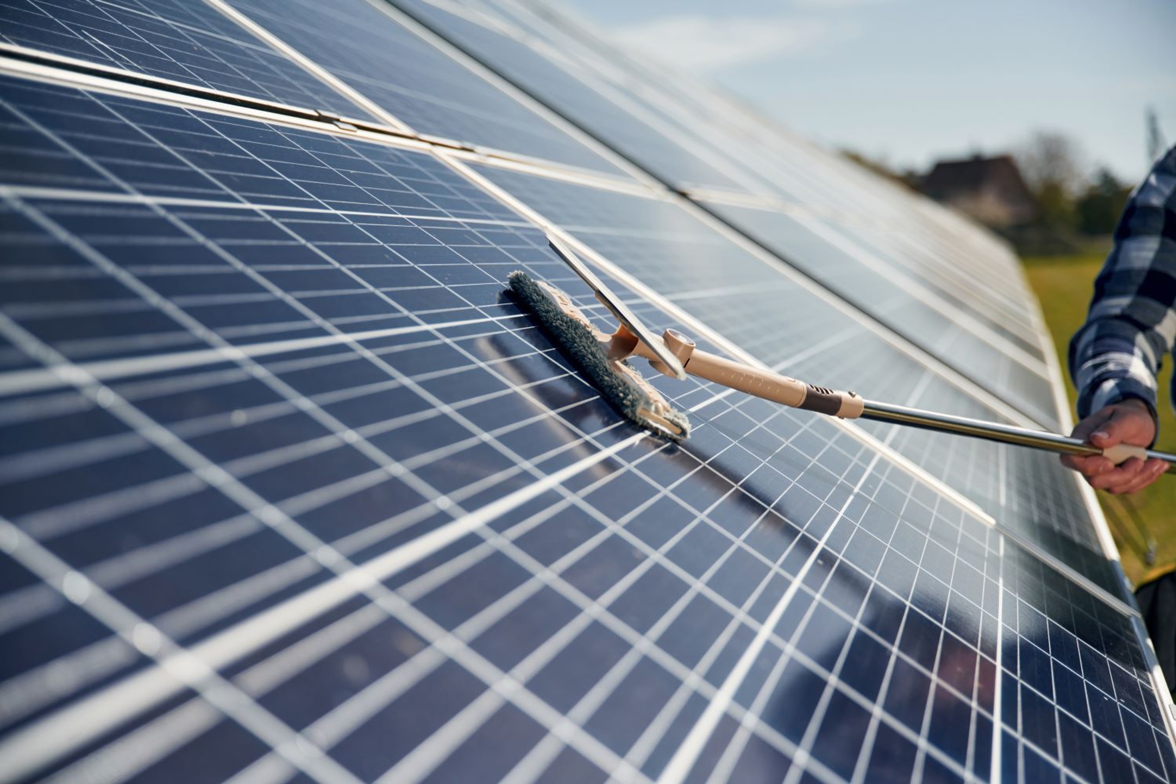 we zien de arm met geruit hemd van iemand die met de borstel/aftrekker zonnepanelen schoonmaakt.