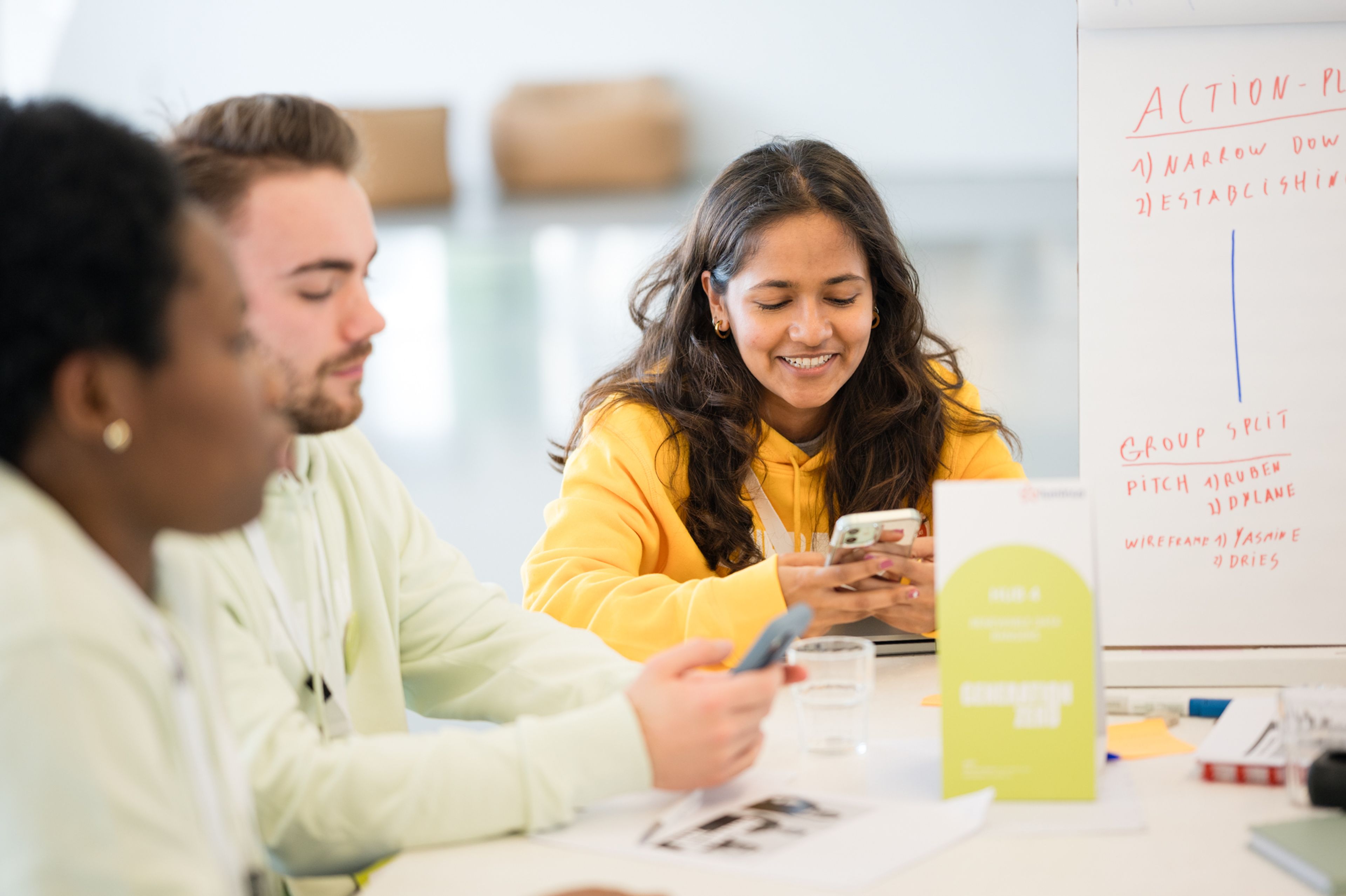 Sanchari met gele hoodie zit lachend op haar phone te kijken.