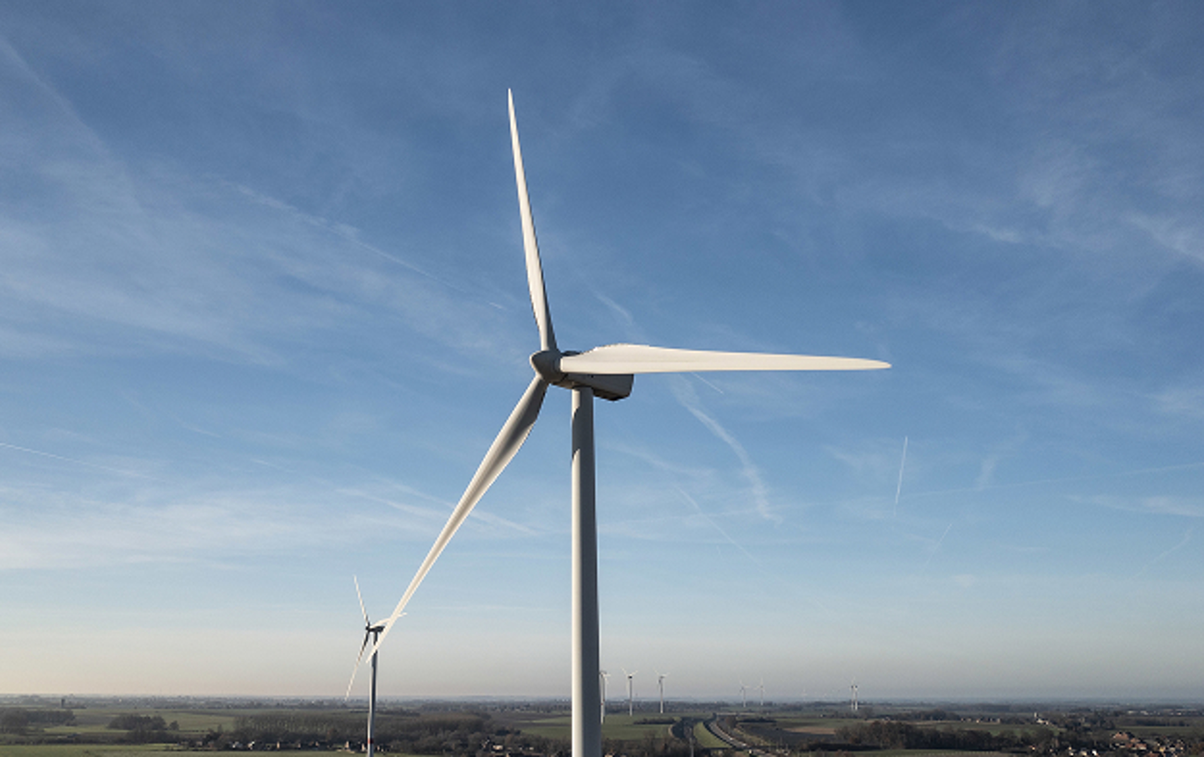 Top van en windturbine tegen blauwe lucht met lichte wolkensluier en zicht op de horizon.