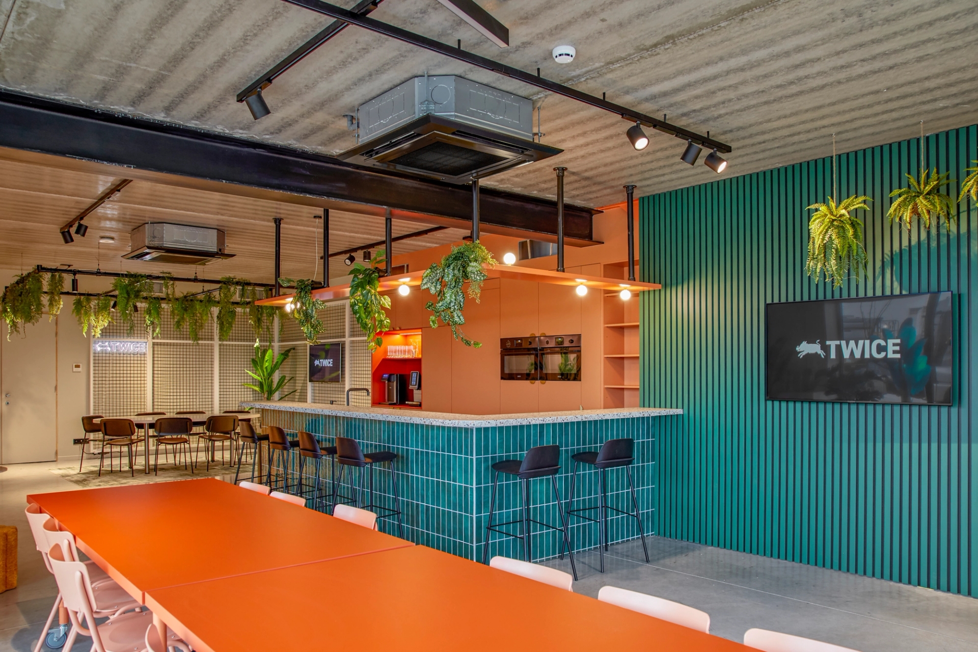Espace de coworking avec bar et grande table orange, équipé de deux modules de pompe à chaleur suspendus au plafond.