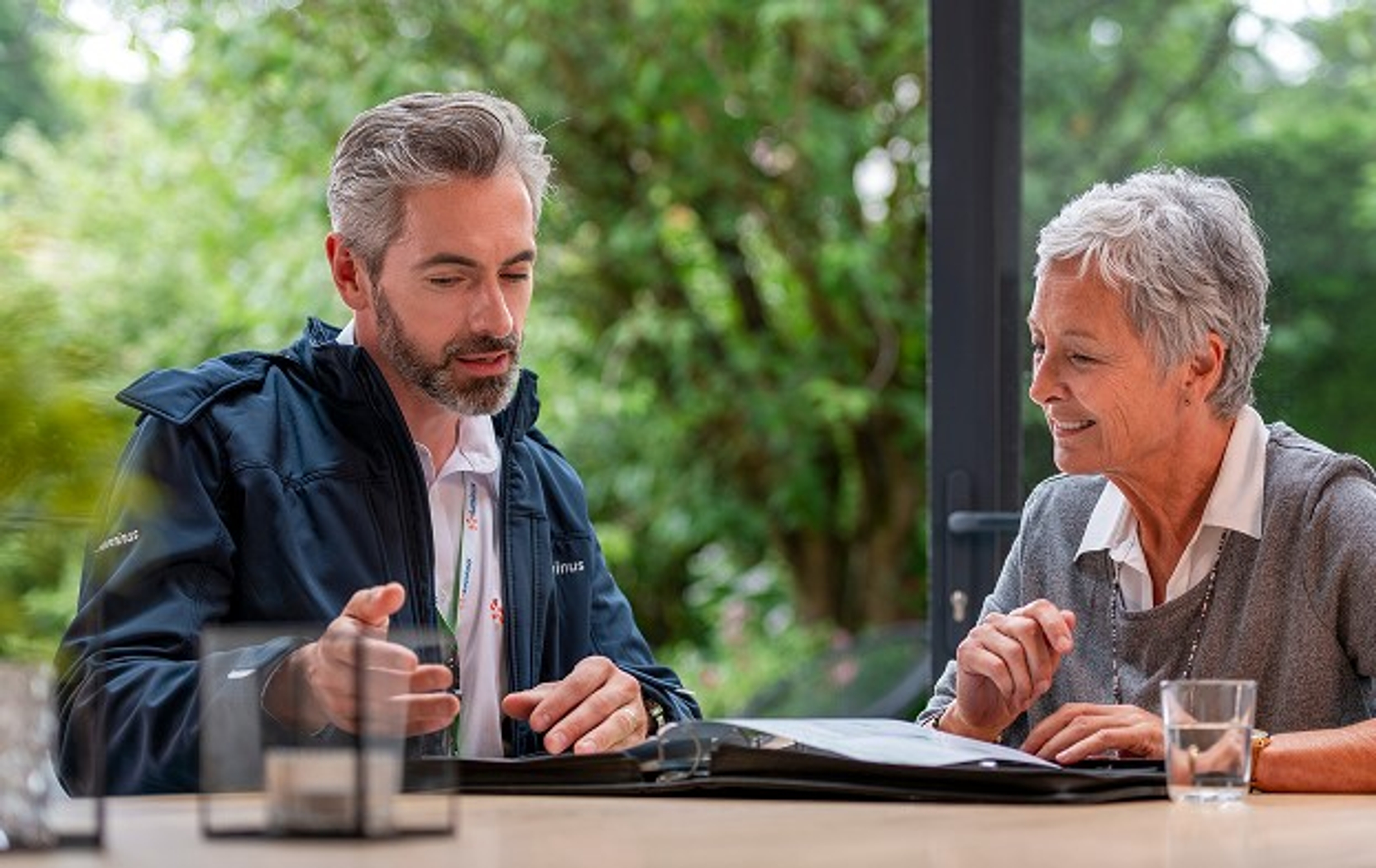 Luminus expert zonnepanelen aan tafel met dame met kort grijs haar, geeft uitleg, openliggende map.