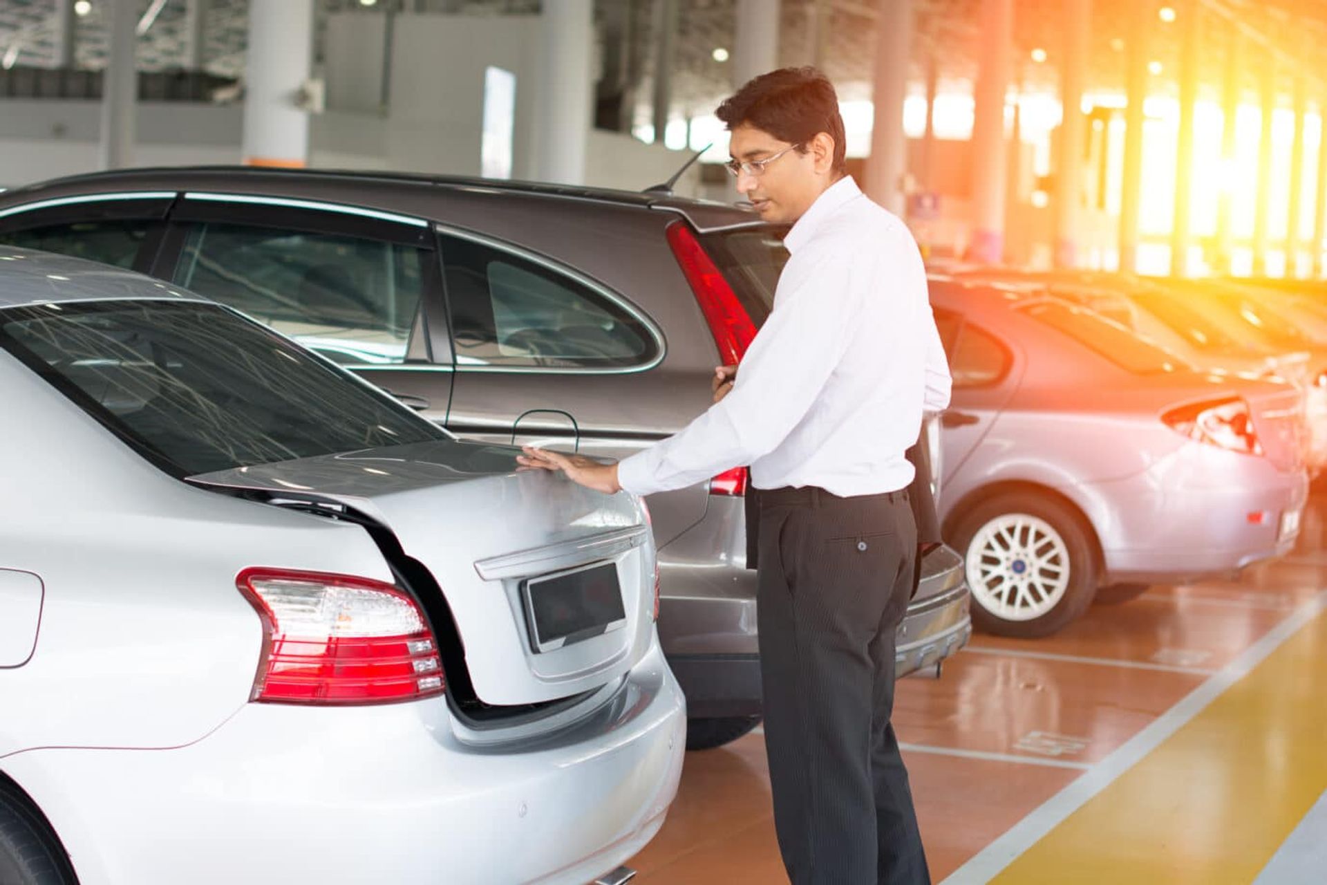 Homme inspectant ou fermant le coffre d'une voiture dans un parking d'entreprise