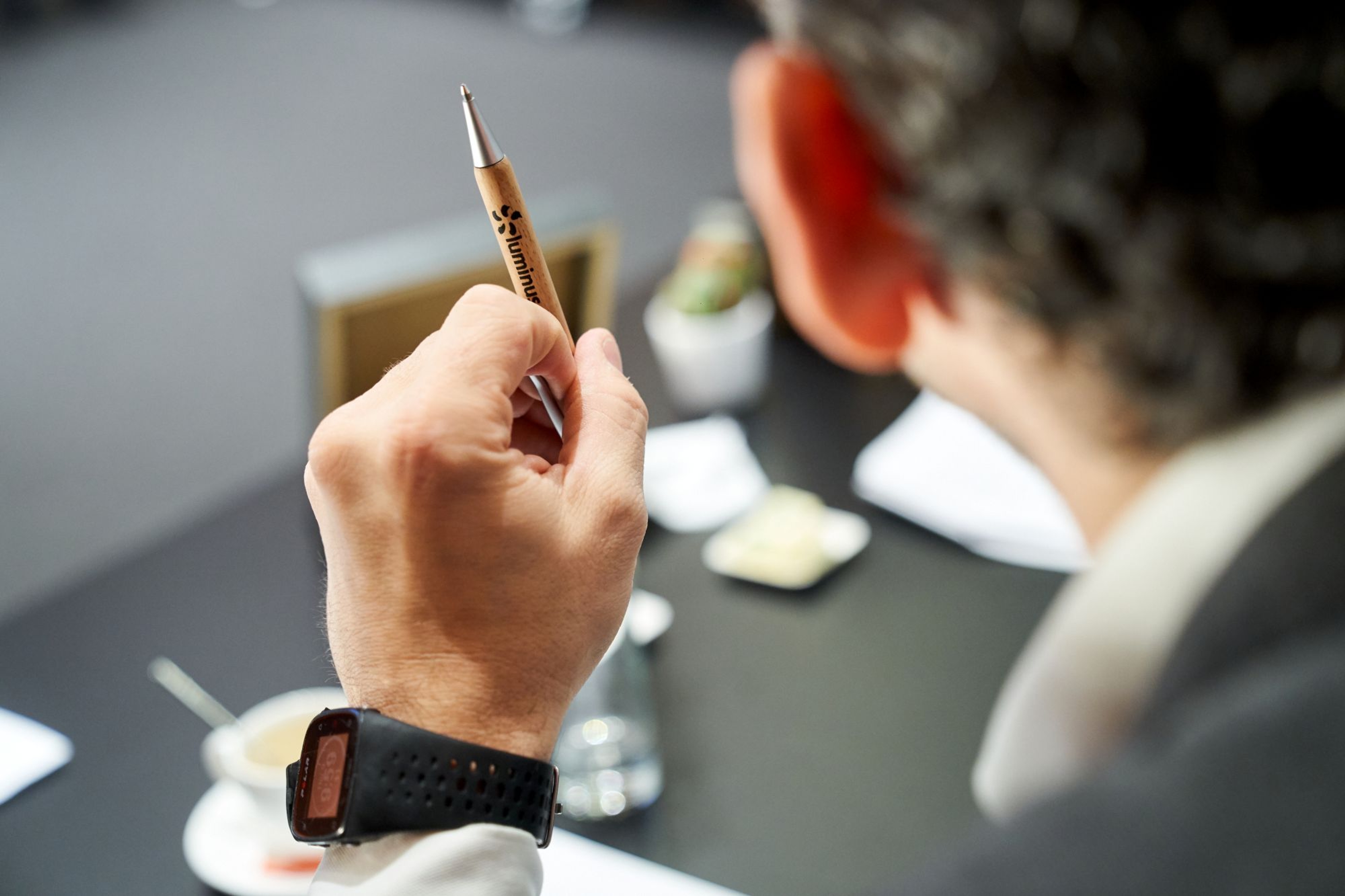 Mannenhand houdt Luminus kogelpen vast in vergaderzaal.