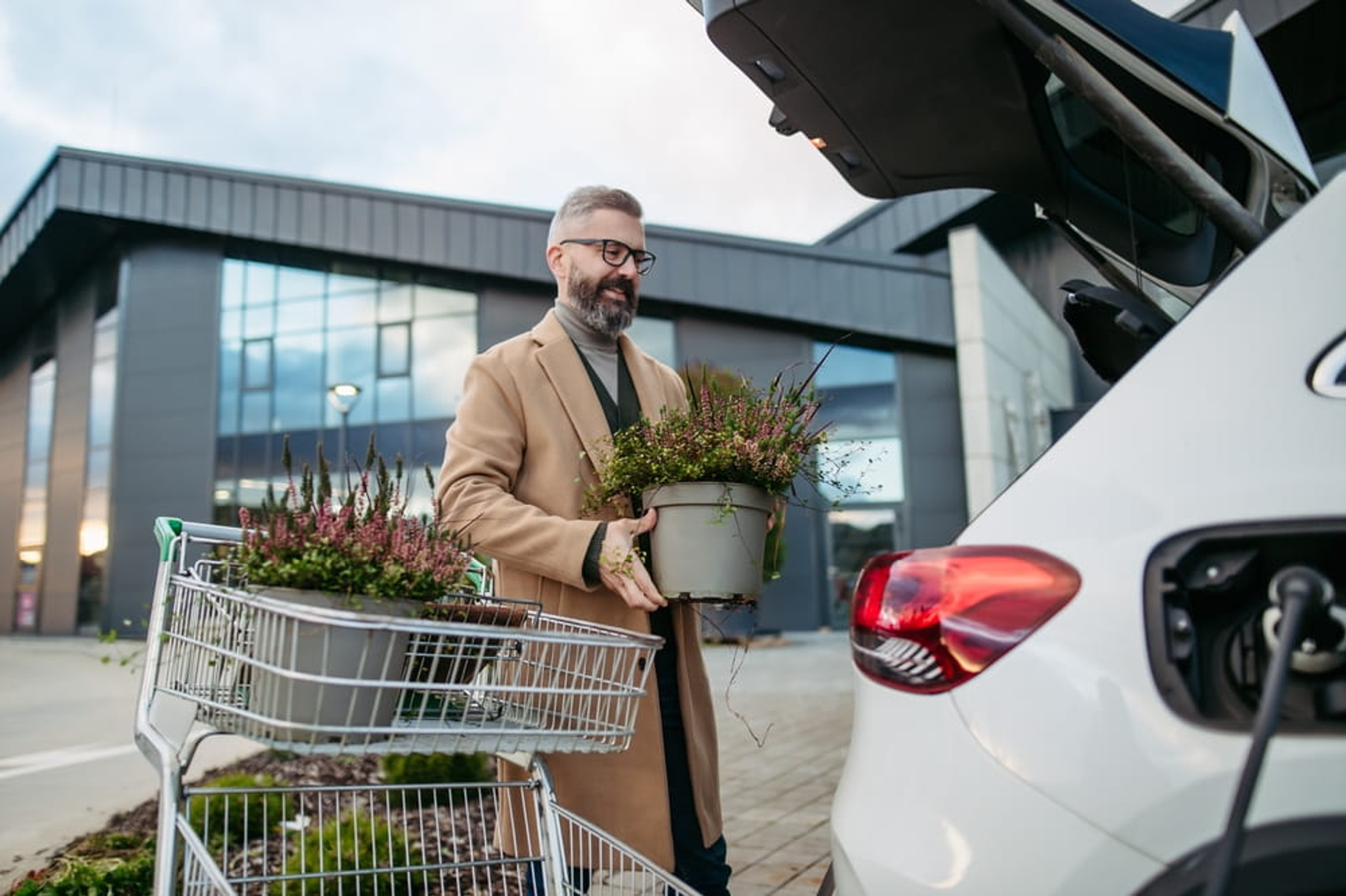 Homme chargeant des plantes dans le coffre d’une voiture électrique sur un parking