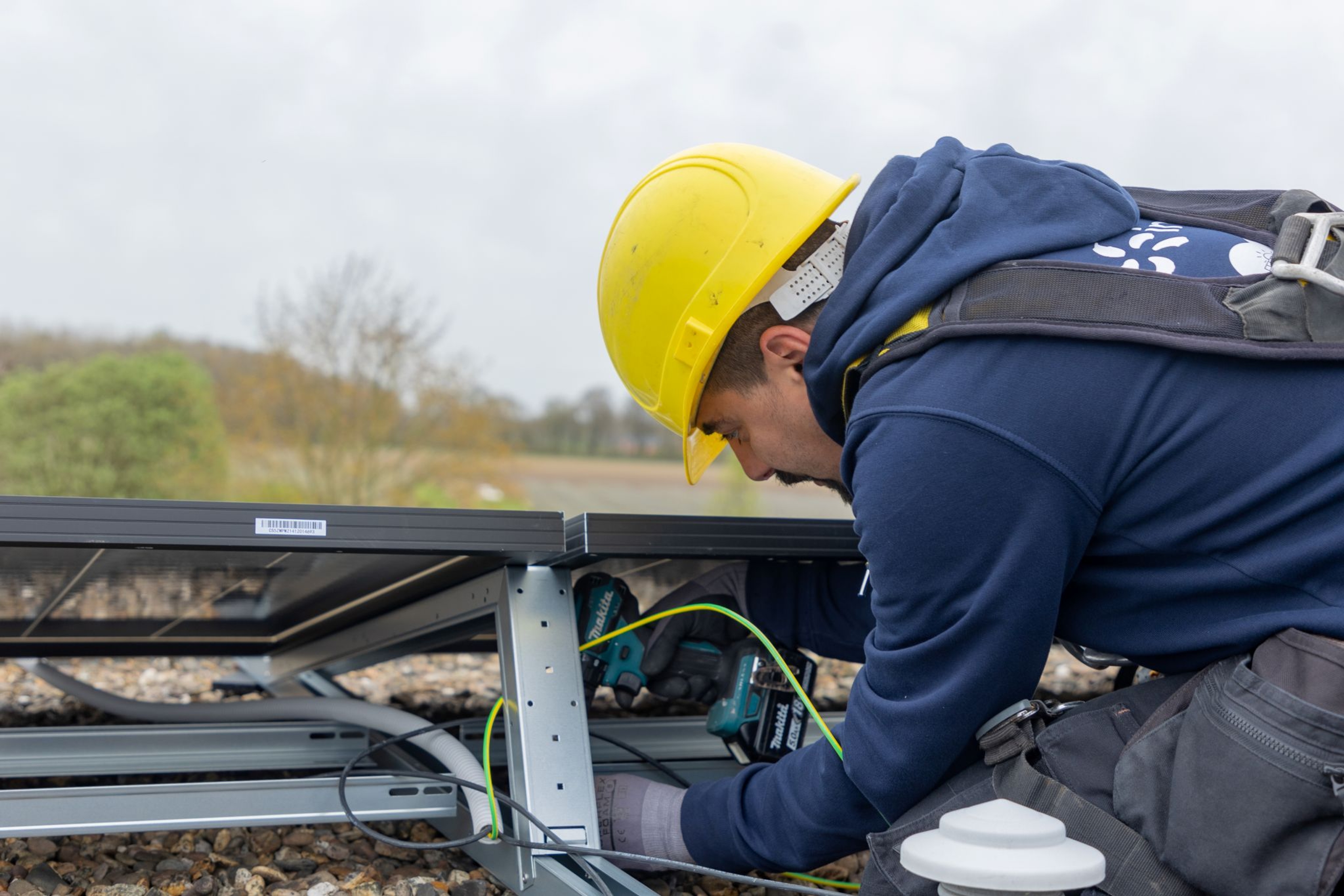 Un technicien portant un casque jaune ajuste un élément sur un panneau solaire installé sur un toit.