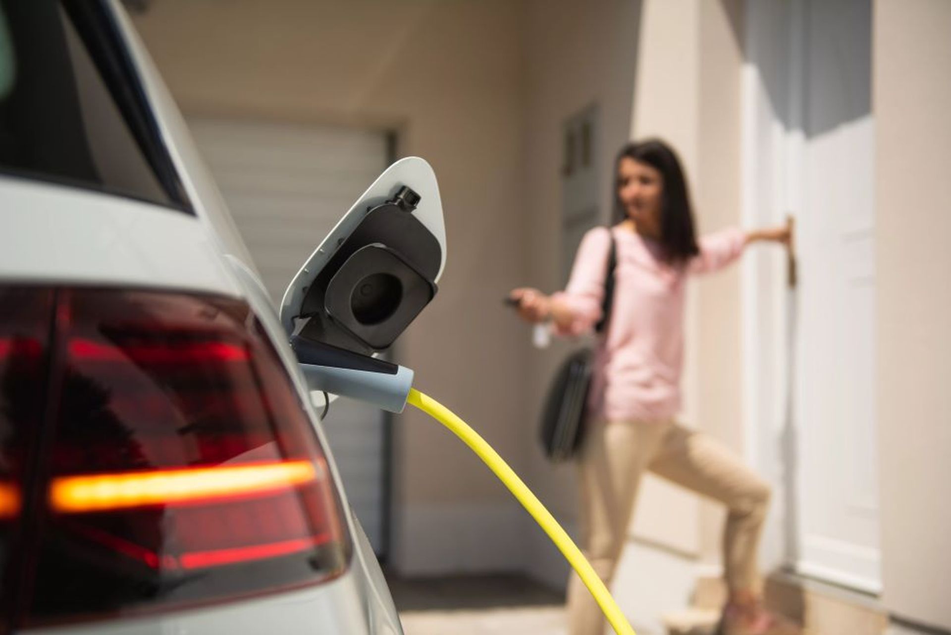 Dame aan haar witte voordeur doet e-wagen op slot die aan het laden is.