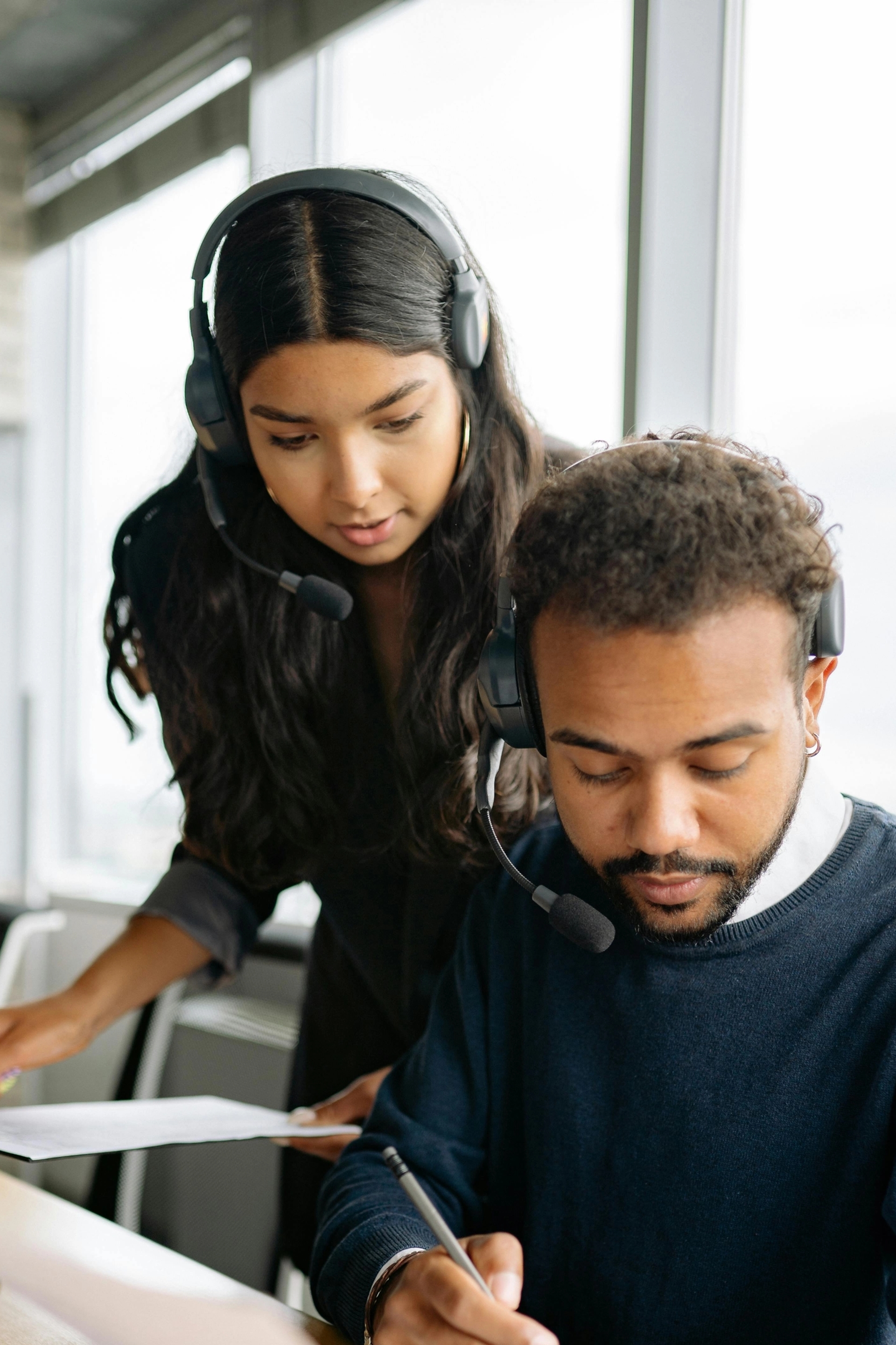 Un homme et une femme portant des casques avec micro collaborent devant un ordinateur, en consultant des documents