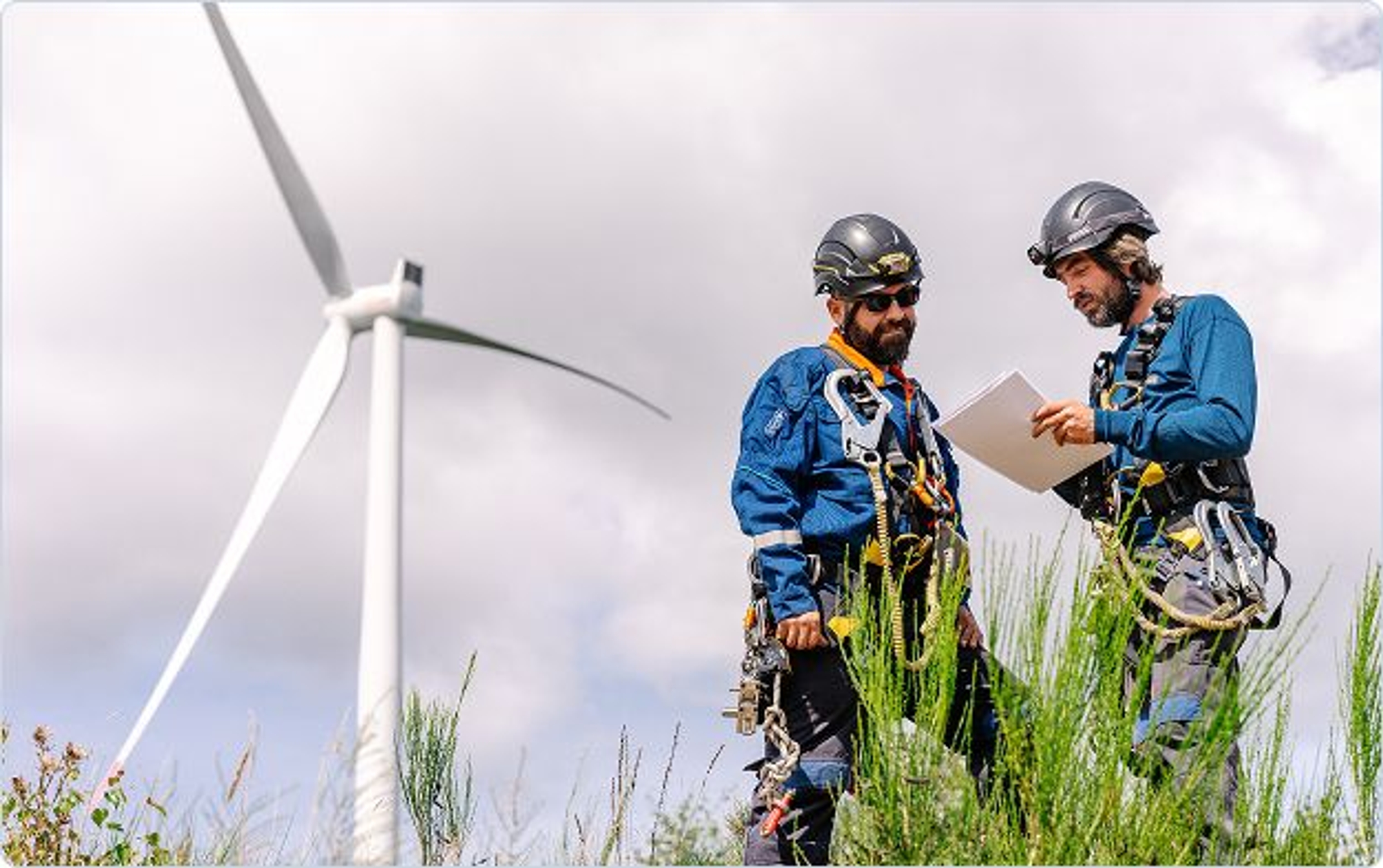 deux techniciens en discussion devant un document avec une éolienne dans le fond