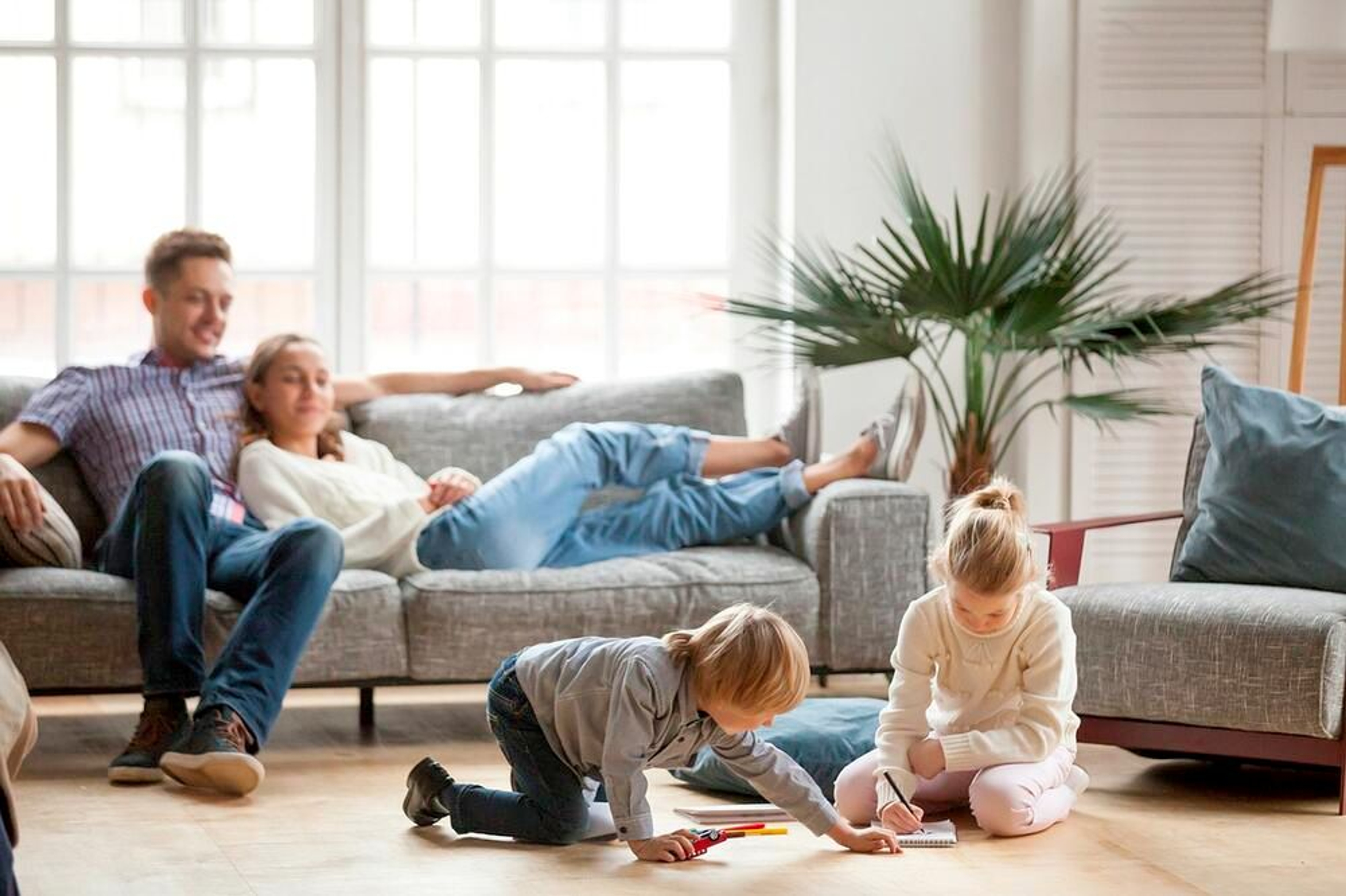 Gezin in de woonkamer: papa zit en mama ligt in de zetel, 2 kindjes spelen op de vloer