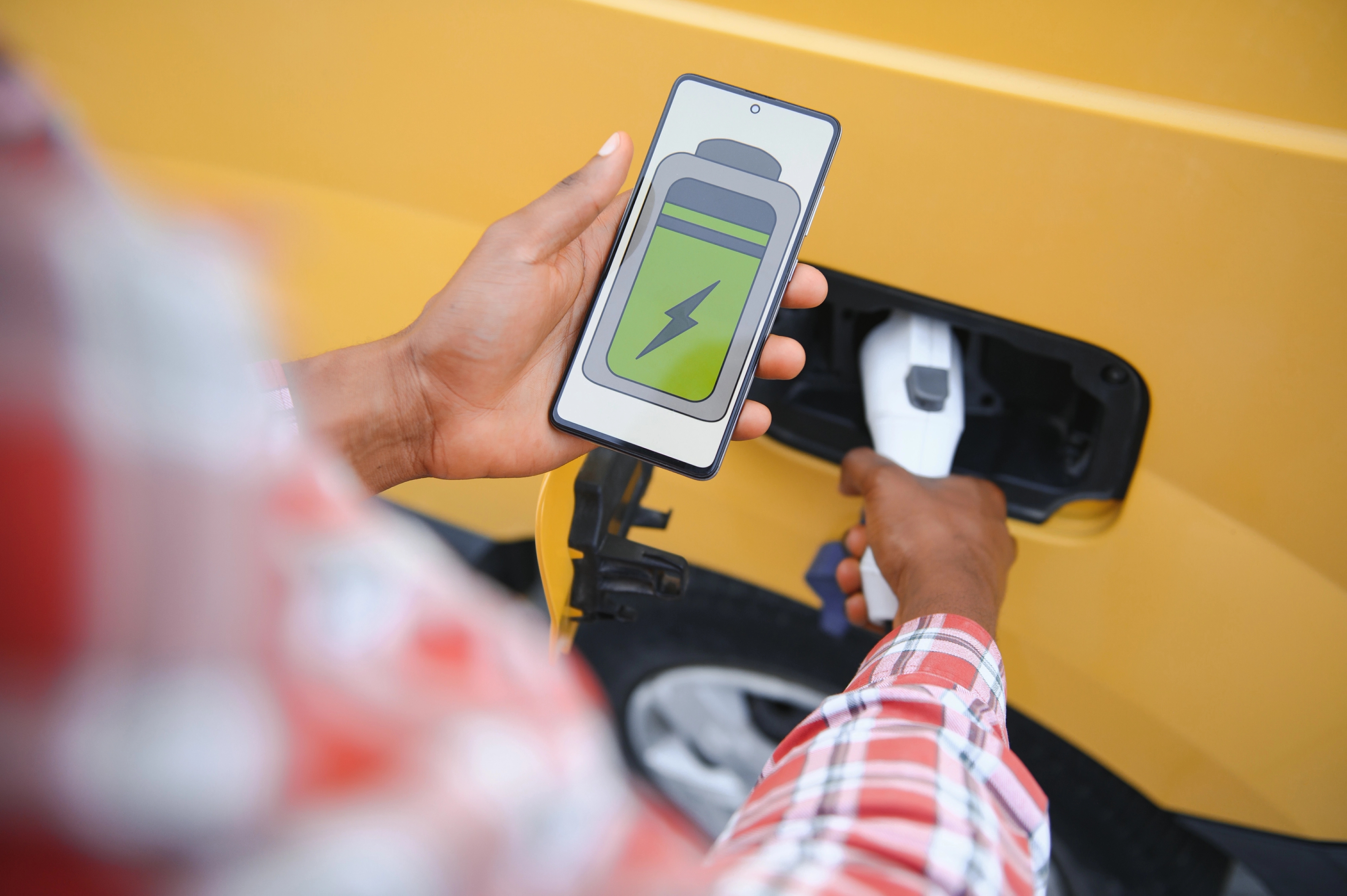 Personne rechargeant un véhicule électrique tout en surveillant le niveau de batterie sur un smartphone