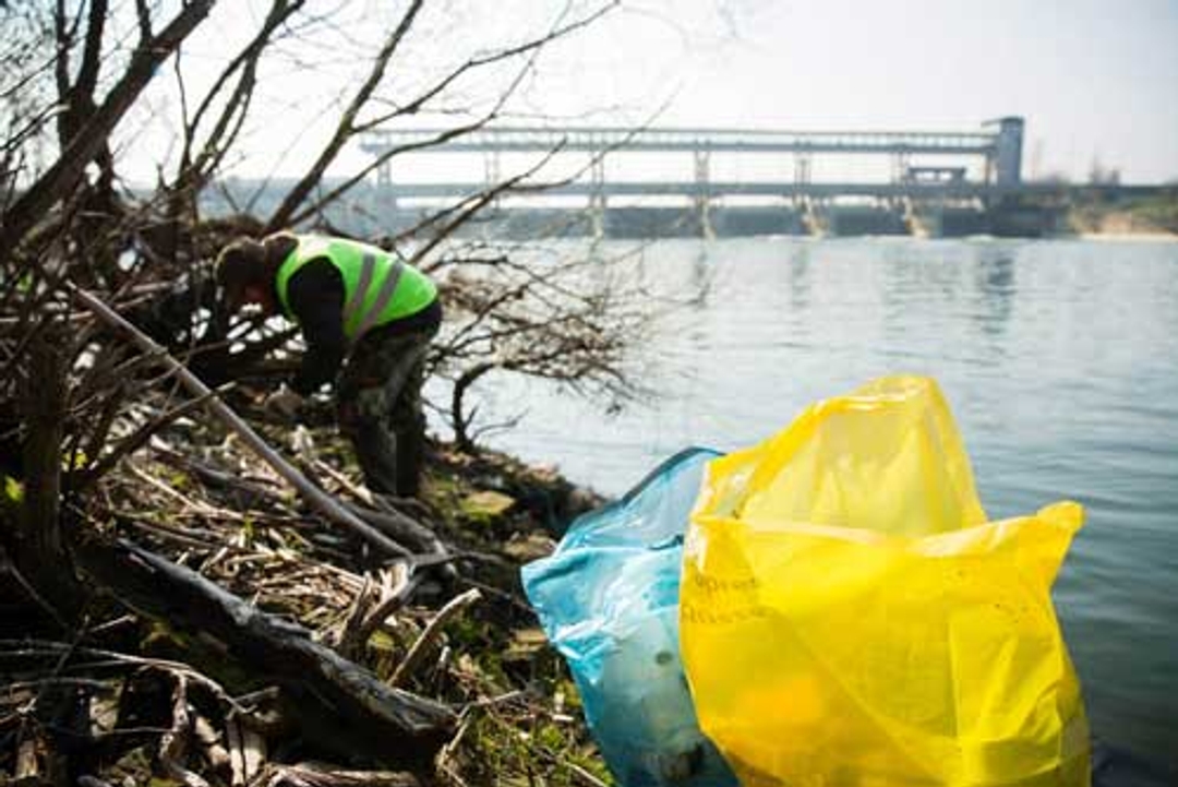 Man op zoek naar afval op de oever van de Maas aan waterkrachtcentrale, gele en blauwe zak