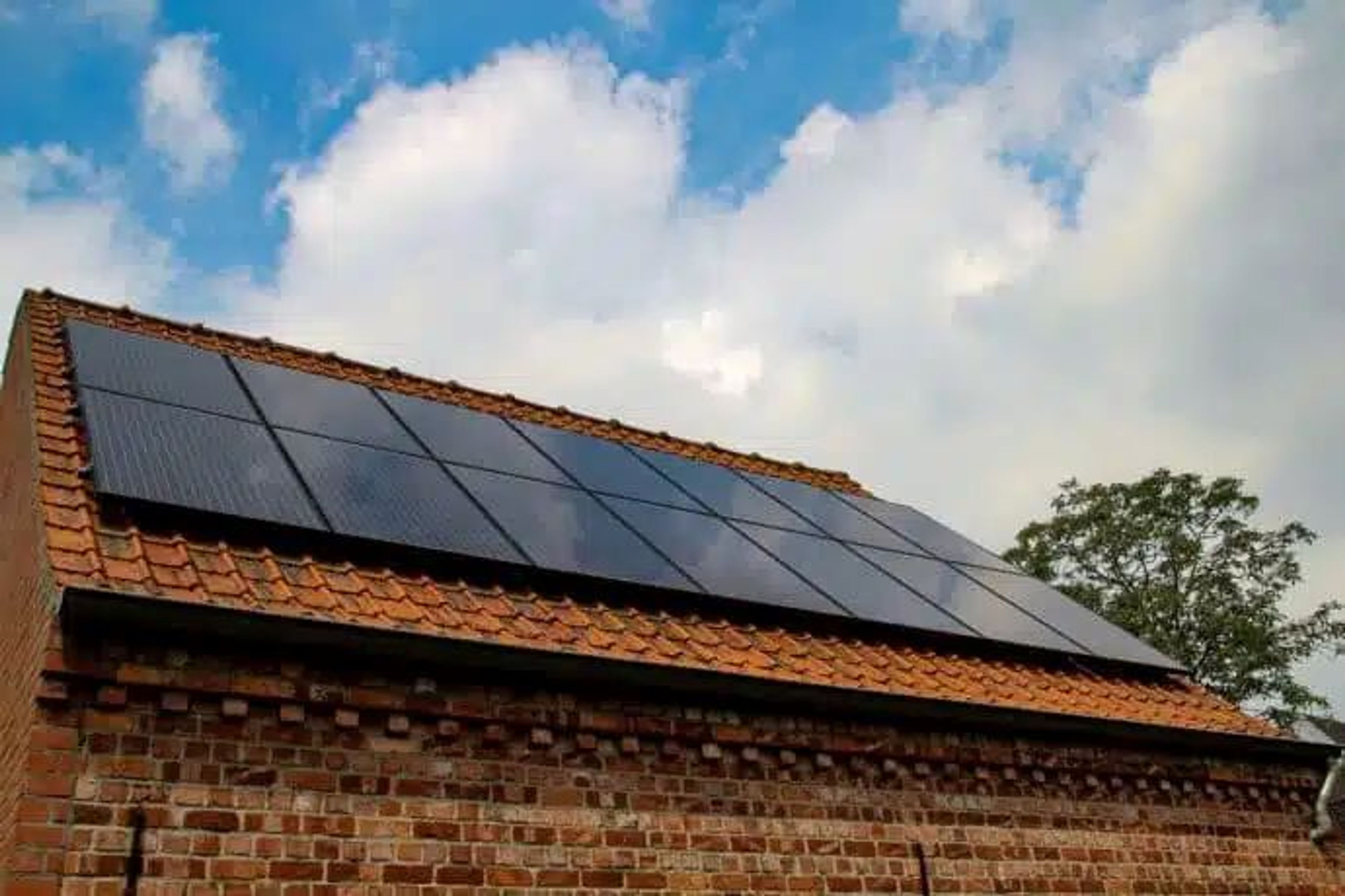 Zonnepanelen op dak van een huis, blauwe lucht met witte wolken