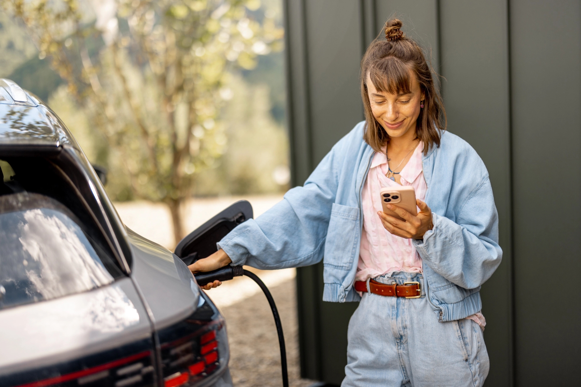 Jongedame kijkt op haar phone terwijl ze de stekker in haar wagen steekt, zwarte muur