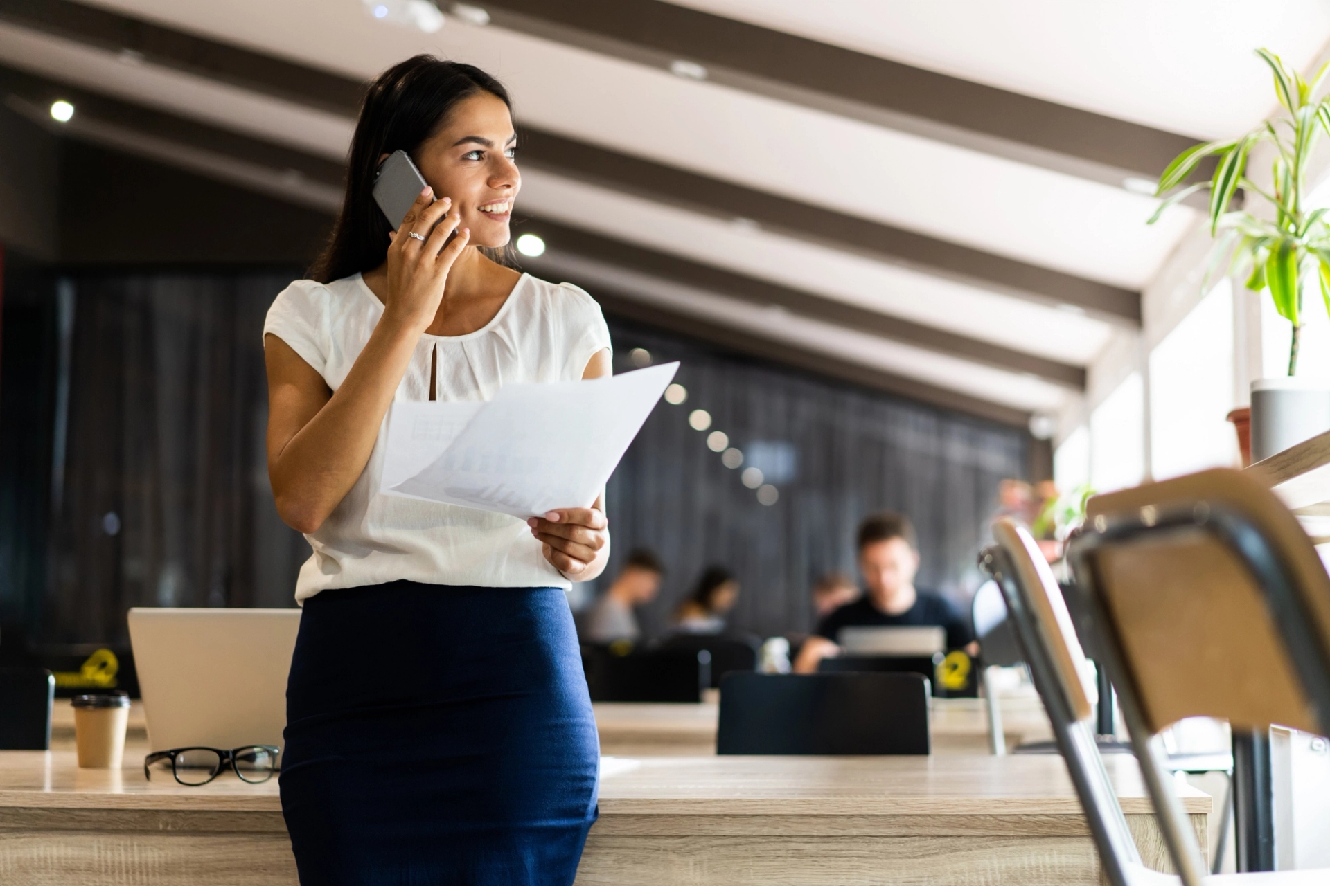 Une dame au bureau, au téléphone, des papiers à la main.