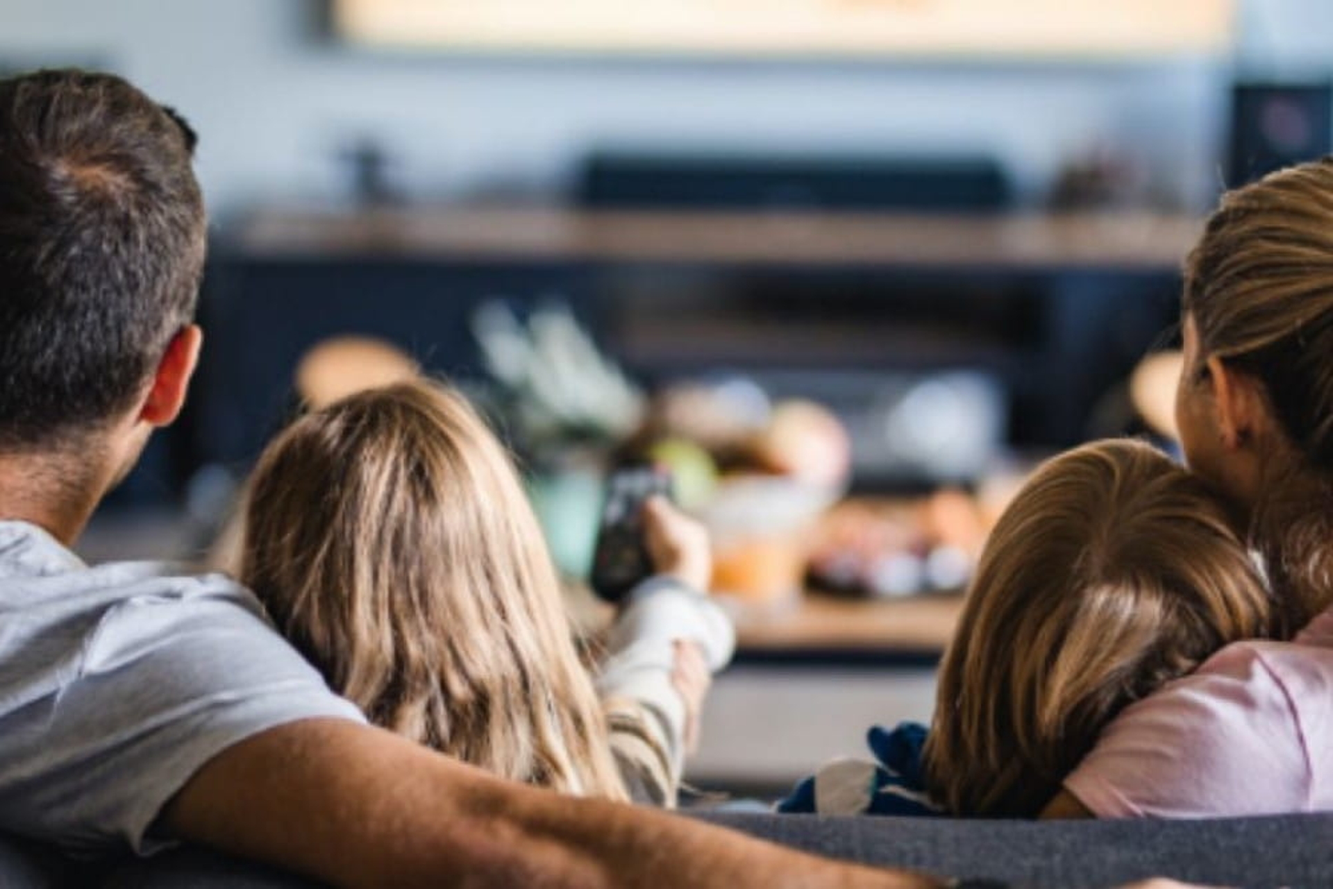 Gezin in de zetel, kijkt tv, meisje zapt, we zien ze langs achter.