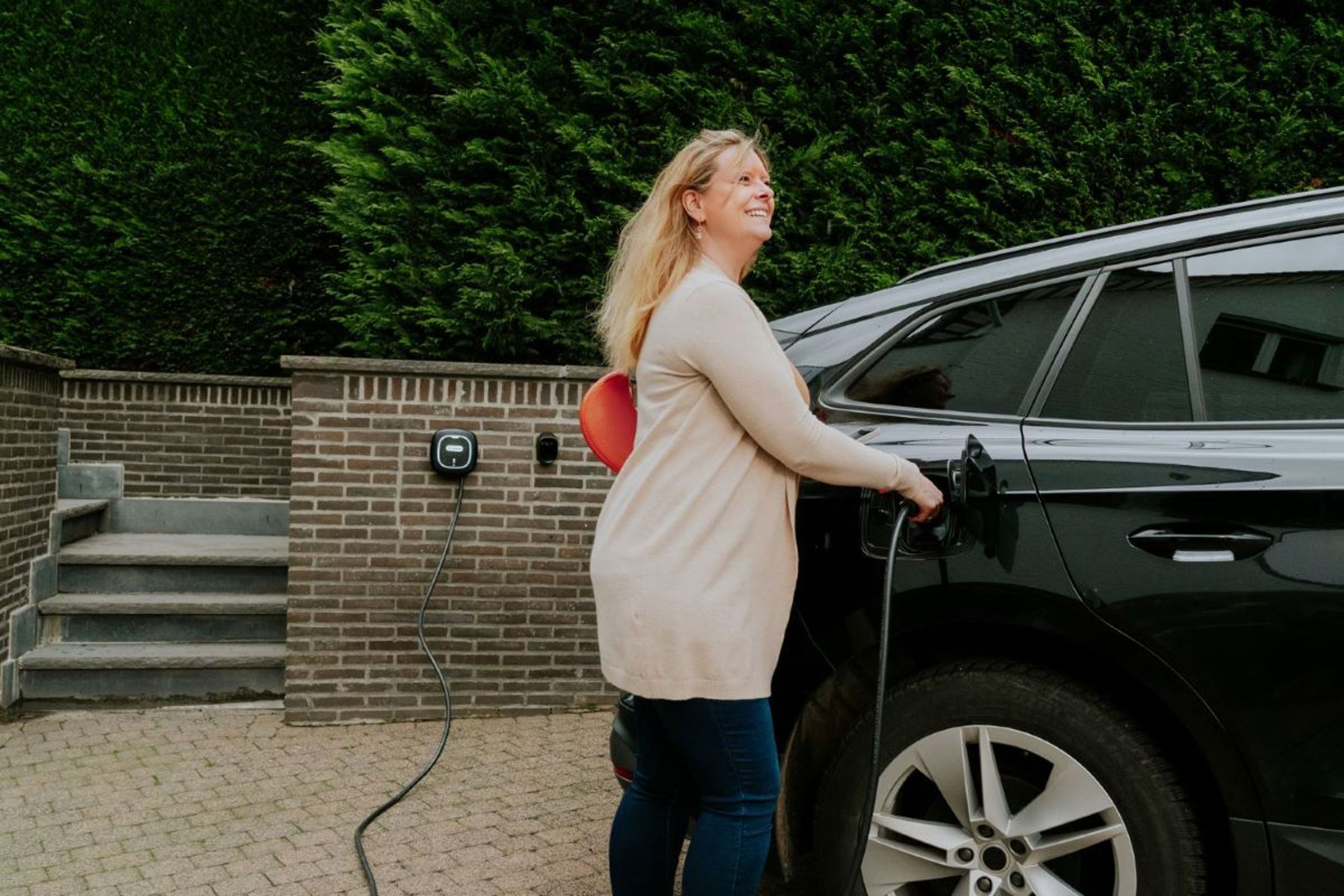 Femme branchant une voiture électrique à une borne de recharge murale installée dans une allée privée