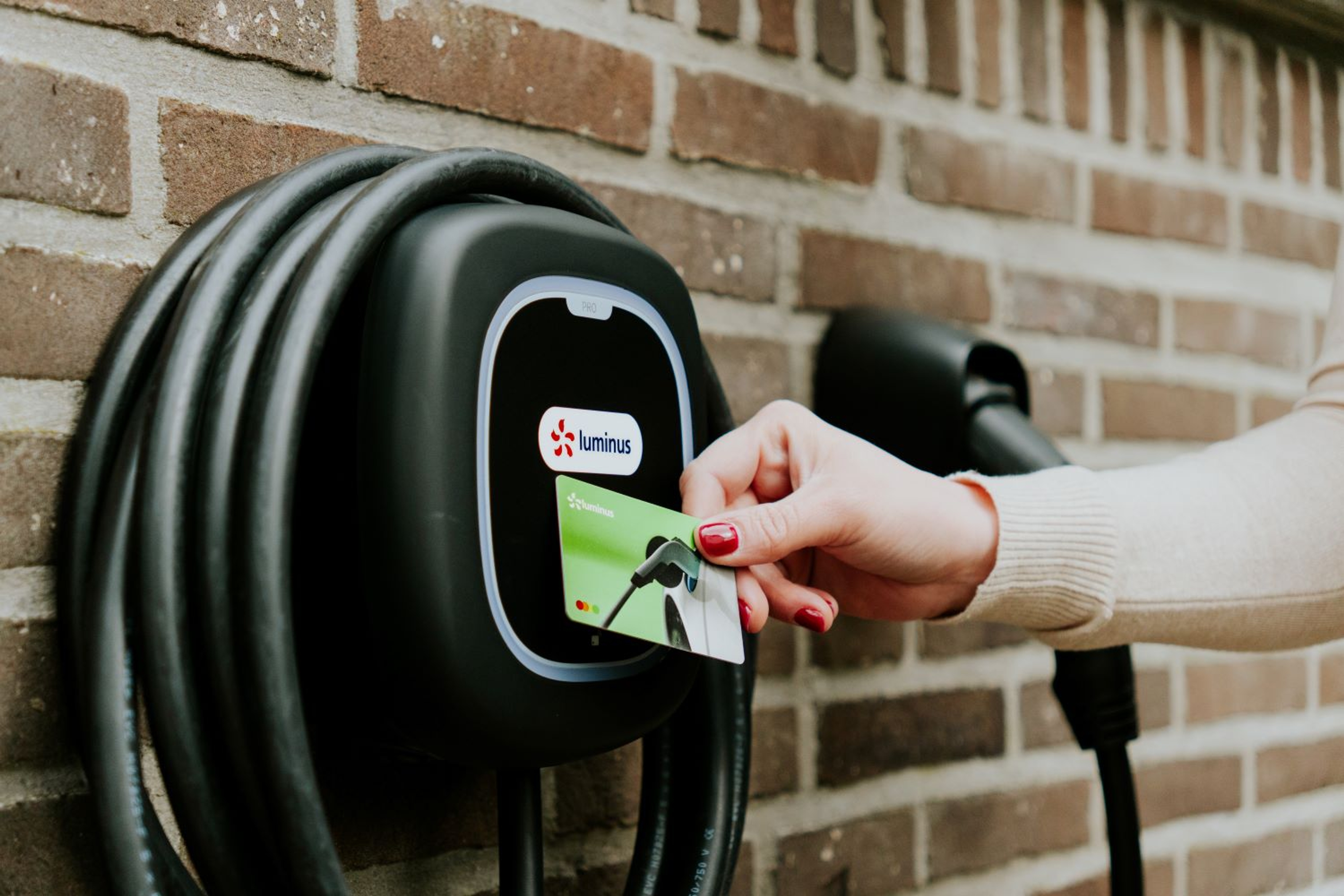 Hand van een dame raakt met de Lumlinus laadpas het schermpje aan van een wallbox laadpunt met zwarte kabel.