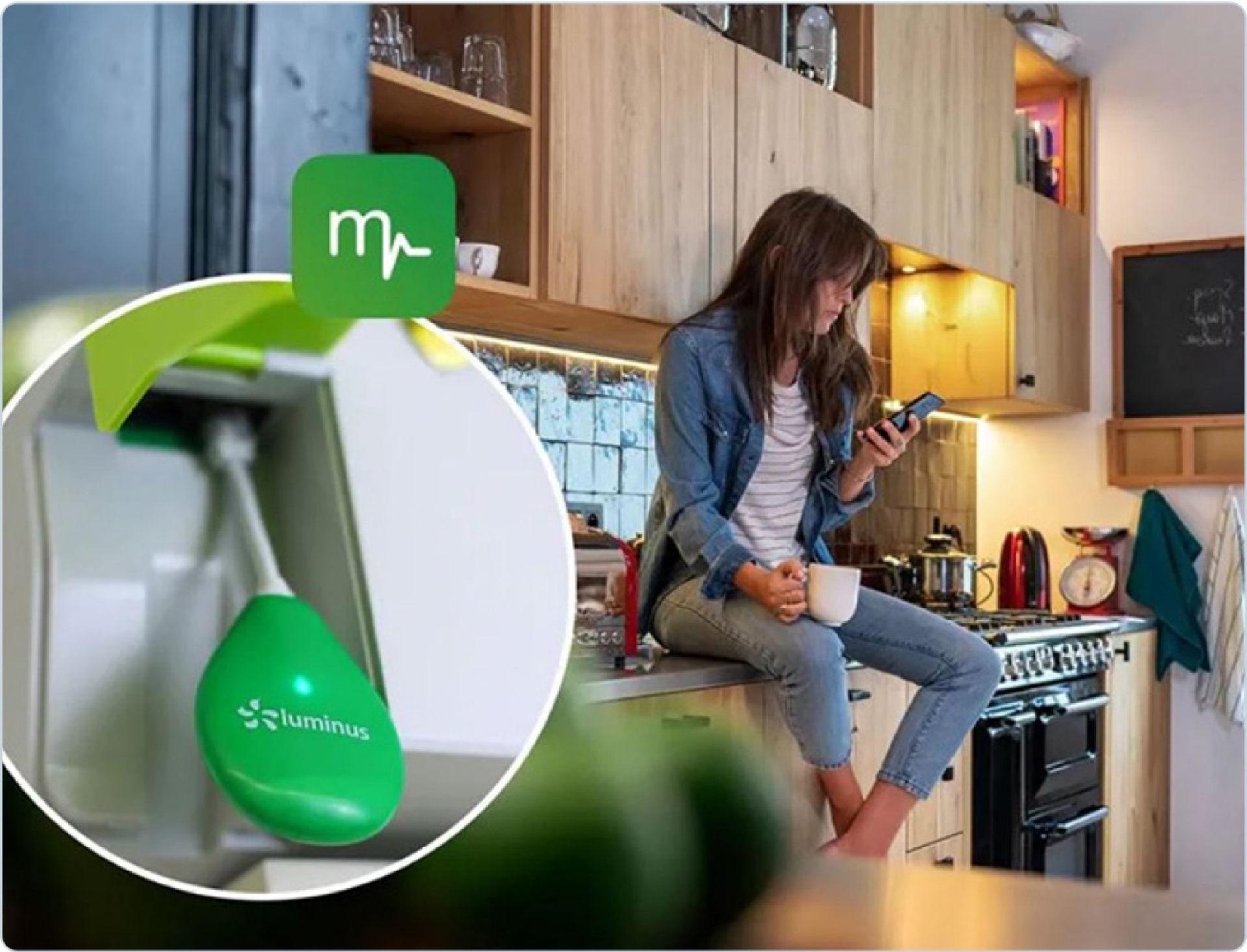 EnergyControl Monitor: jonge vrouw zit op het aanrecht in de keuken en kijkt op haar phone, kopje in de andere hand. Inzetfoto: de dongle die je in je digitale meter klikt.