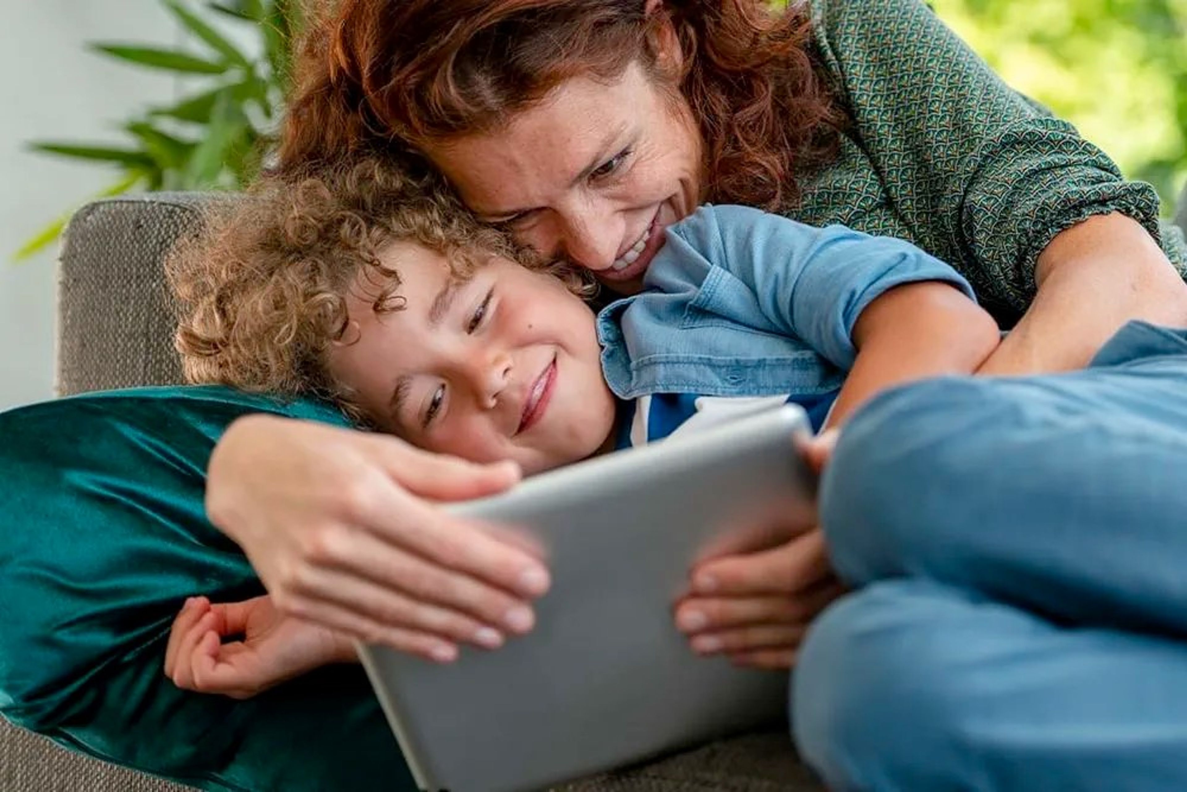 Mama en zoontje in de zetel knuffelen en kijken op de tablet