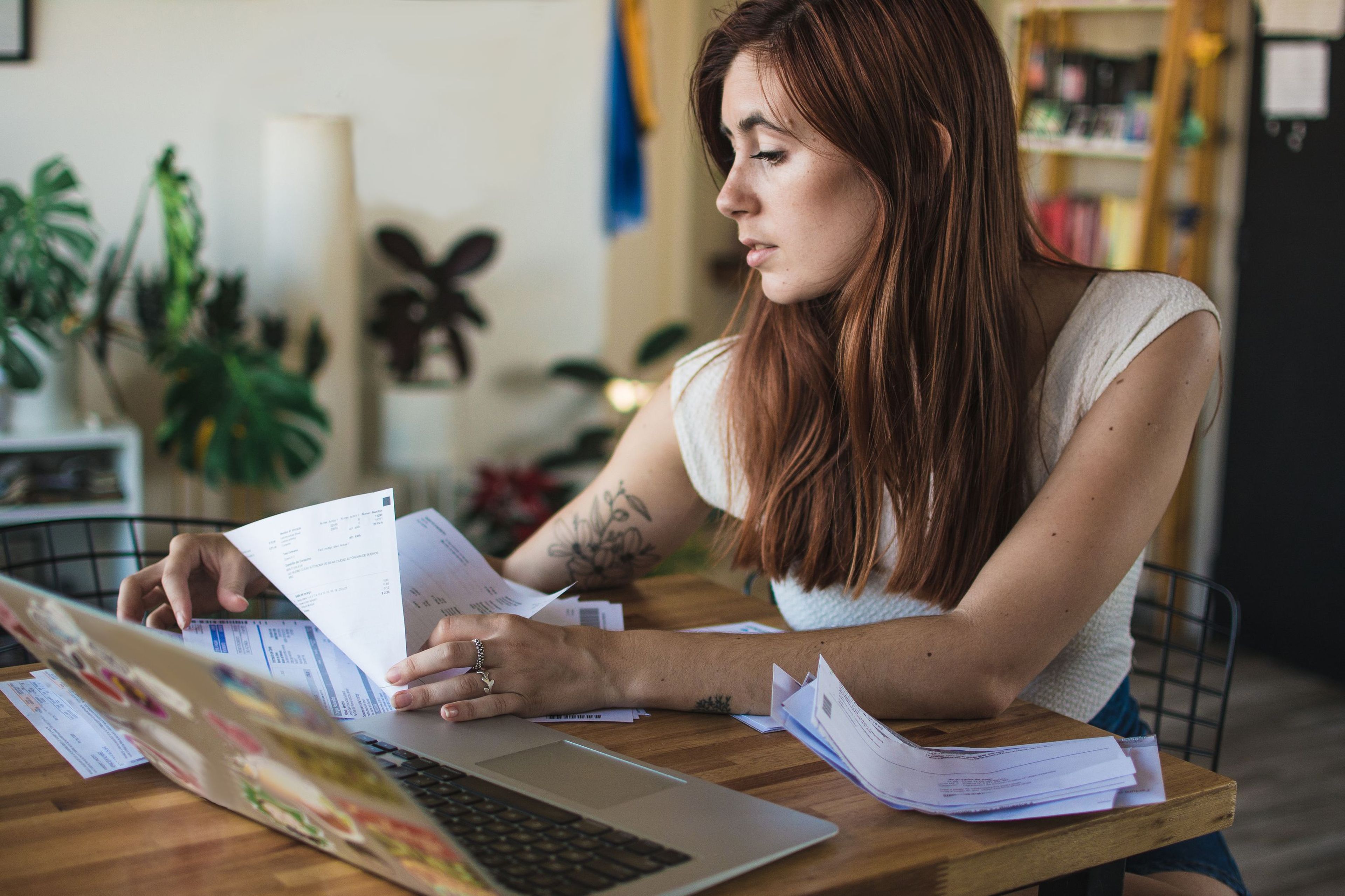 Jonge vrouw aan tafel met laptop en facturen/papieren