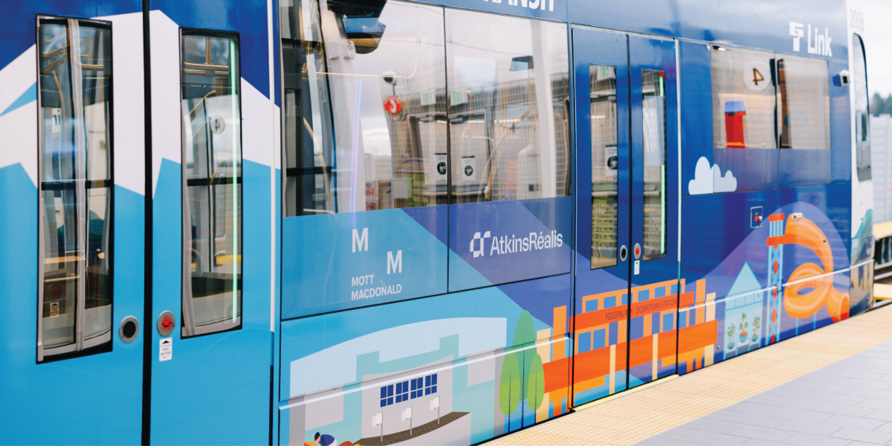 Close-up of a Sound Transit Link Light Rail train featuring a colorful illustrated wrap showing a Seattle cityscape and mountains
