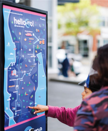 Child pointing at a large illustrated Sound Transit "hello!" Link Light Rail system map display at the opening event