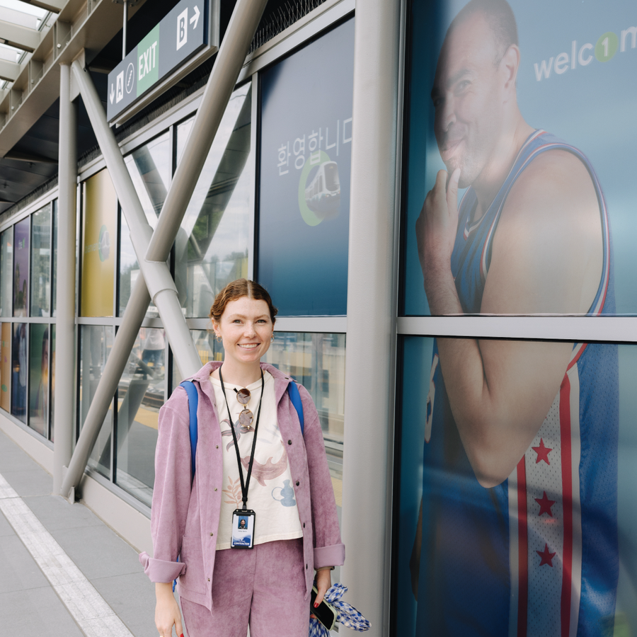 Designer smiling at a Sound Transit Link Light Rail station with large community mural artwork visible in the background